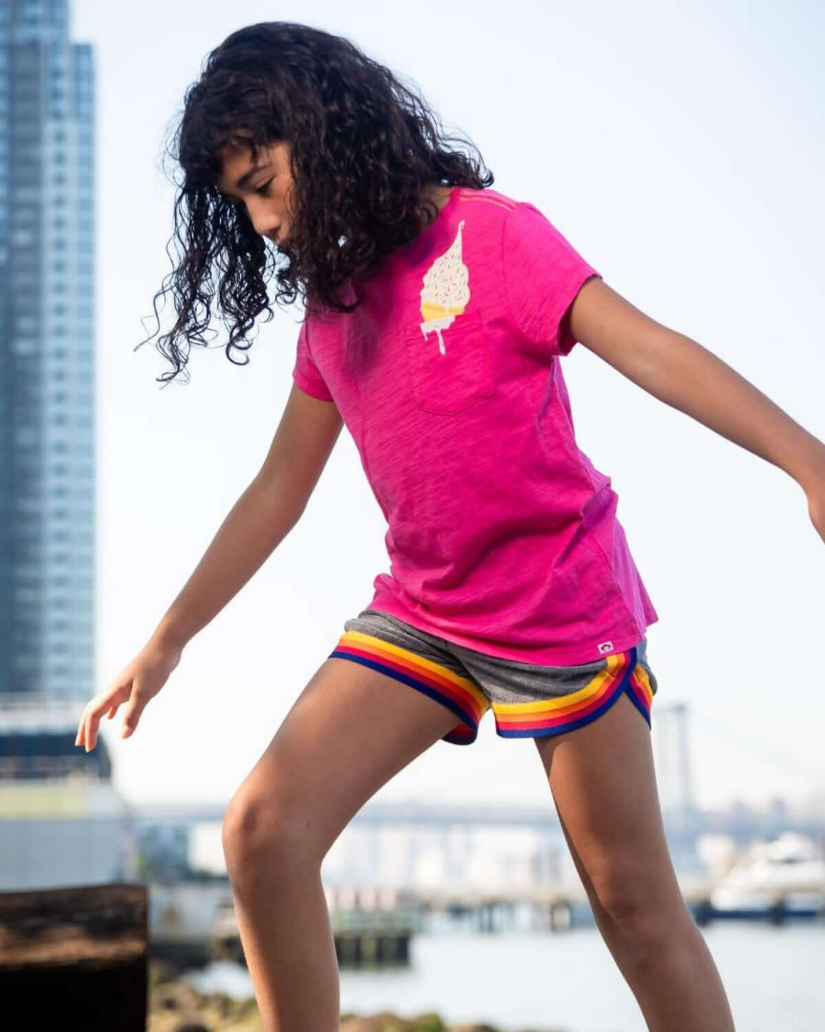 A cheerful girl wearing a Fuchsia Ice Cream Tee and colorful shorts, enjoying a playful day outdoors.
