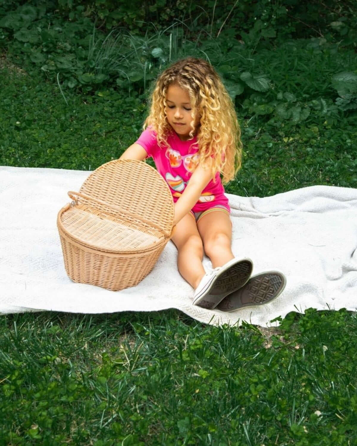 Little girl in a playful pink tee exploring a picnic basket on a sunny day—stylish kids clothes for adventurous spirits!