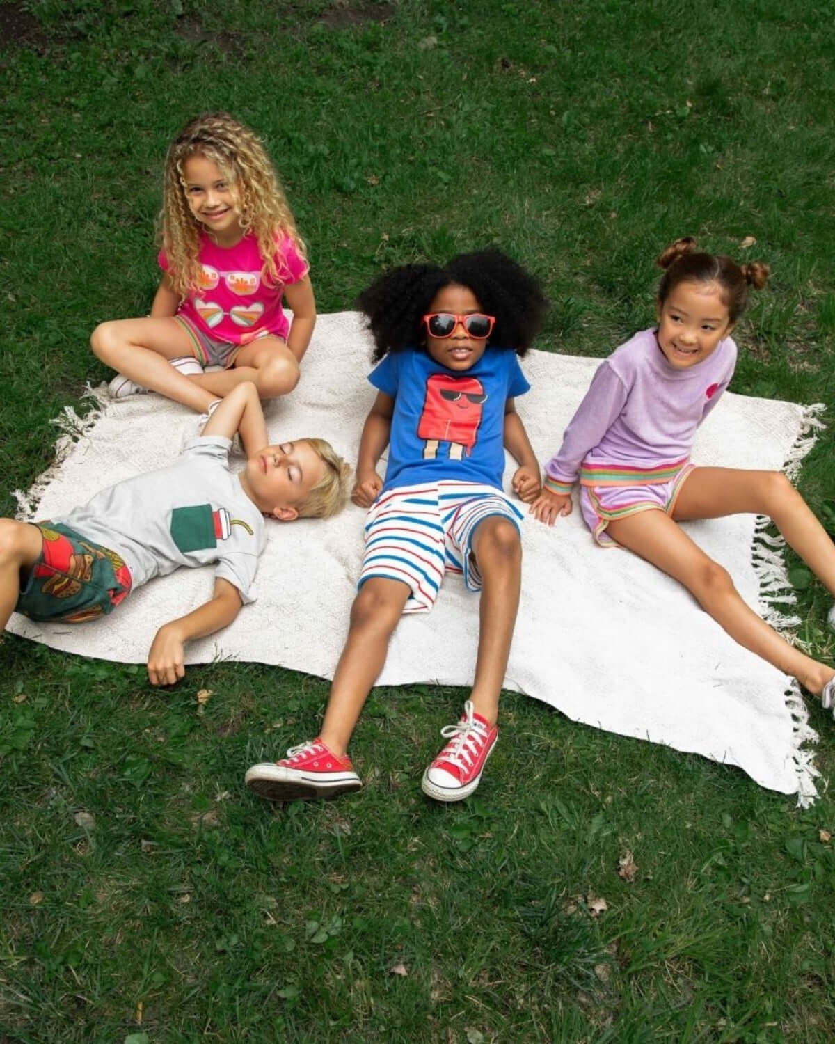 A cheerful group of kids in vibrant Appaman outfits enjoying a sunny day on a blanket, radiating playful spring vibes.