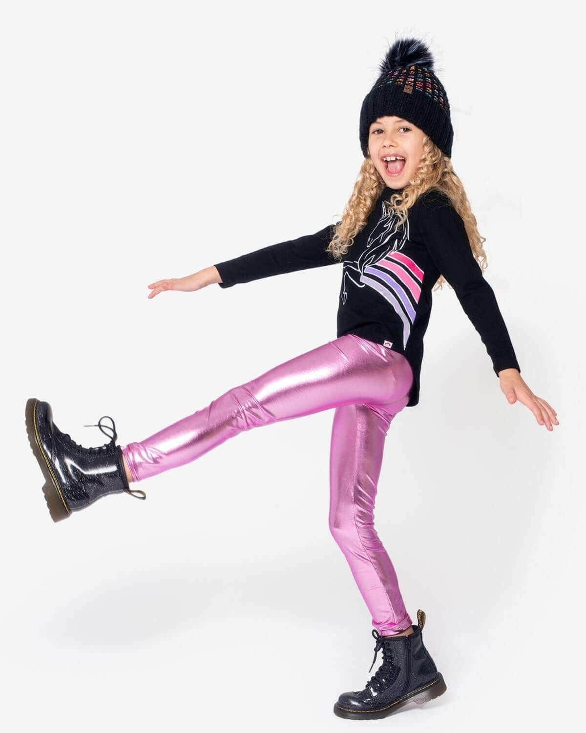 A girl joyfully posing in shiny pink leggings and a stylish black tee, showcasing vibrant kids clothes for confident play!