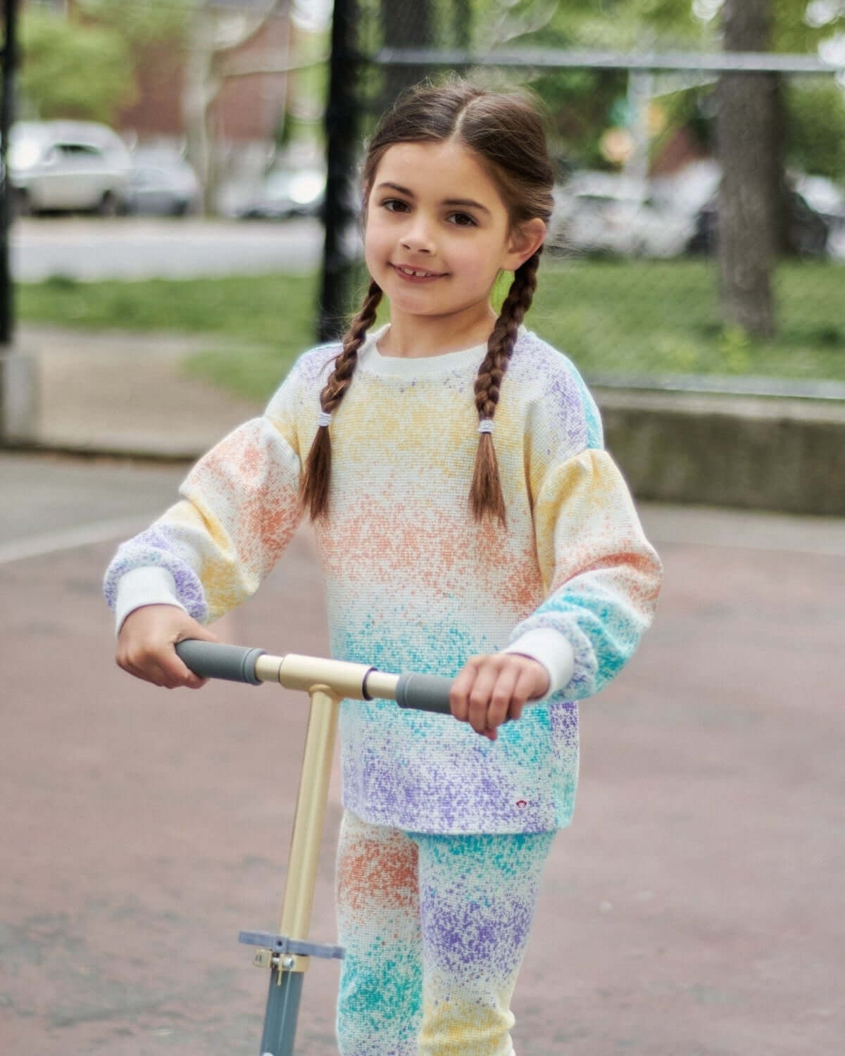 Stylish girl scooting in colorful splatter print outfit, showcasing high-quality kids clothes for playful moments.