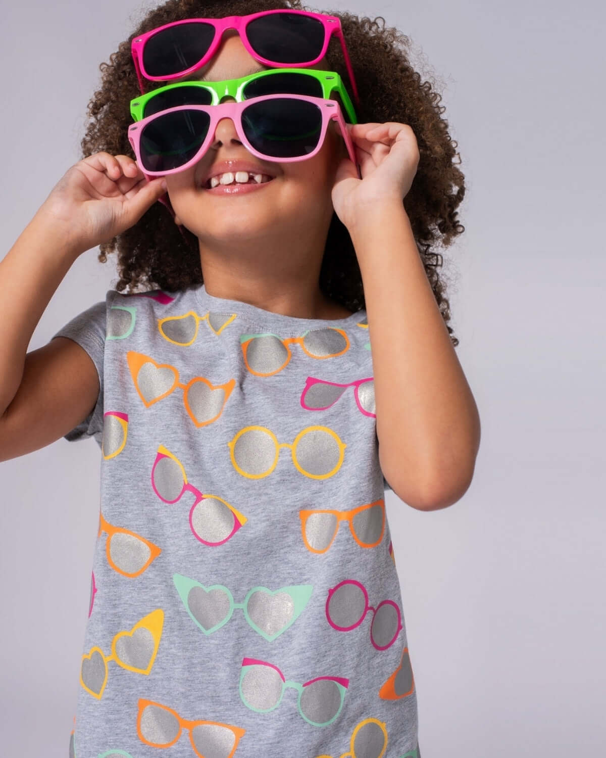 Stylish girl in a light grey t-shirt with fun sunglasses print, showcasing vibrant summer fun in kids clothes!