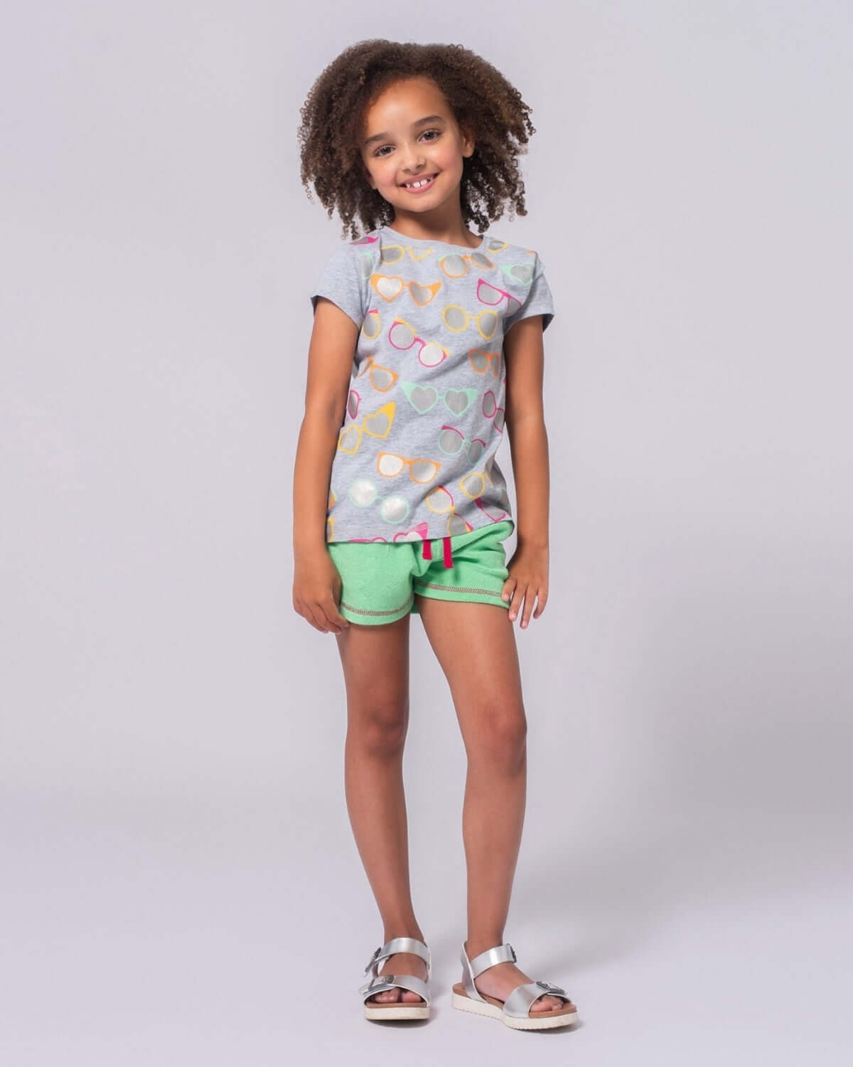 Little girl rocking a light grey sunglasses tee, staying cool and stylish in cute green shorts for back to school adventures!