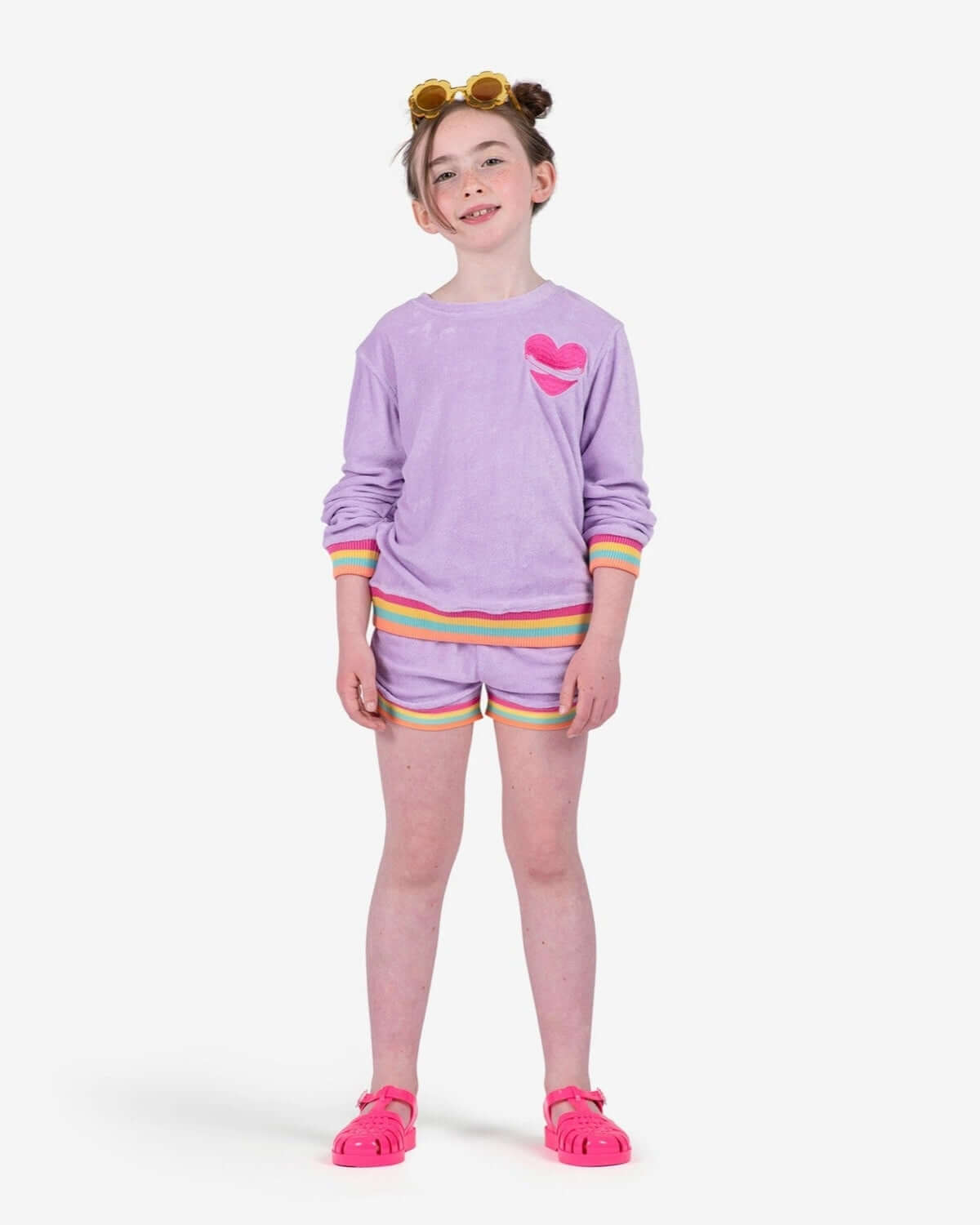A stylish young girl poses in a Sweet Lavender Ruby Sweatshirt, showcasing fun rainbow details—perfect for vibrant kids clothes!