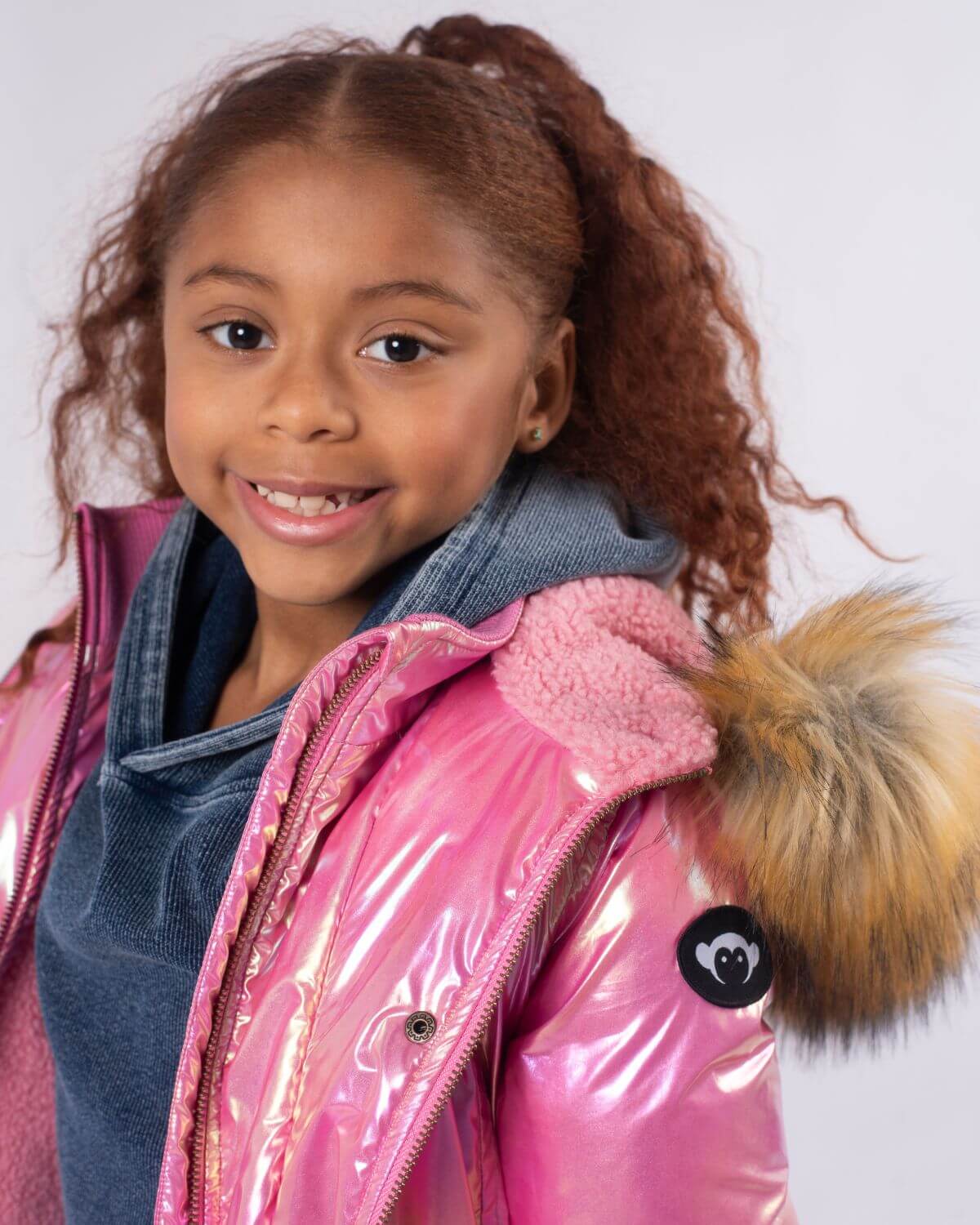 Bright-eyed girl sporting a radiant pink Middie Puffer Coat with faux fur trim, perfect for stylish winter adventures.
