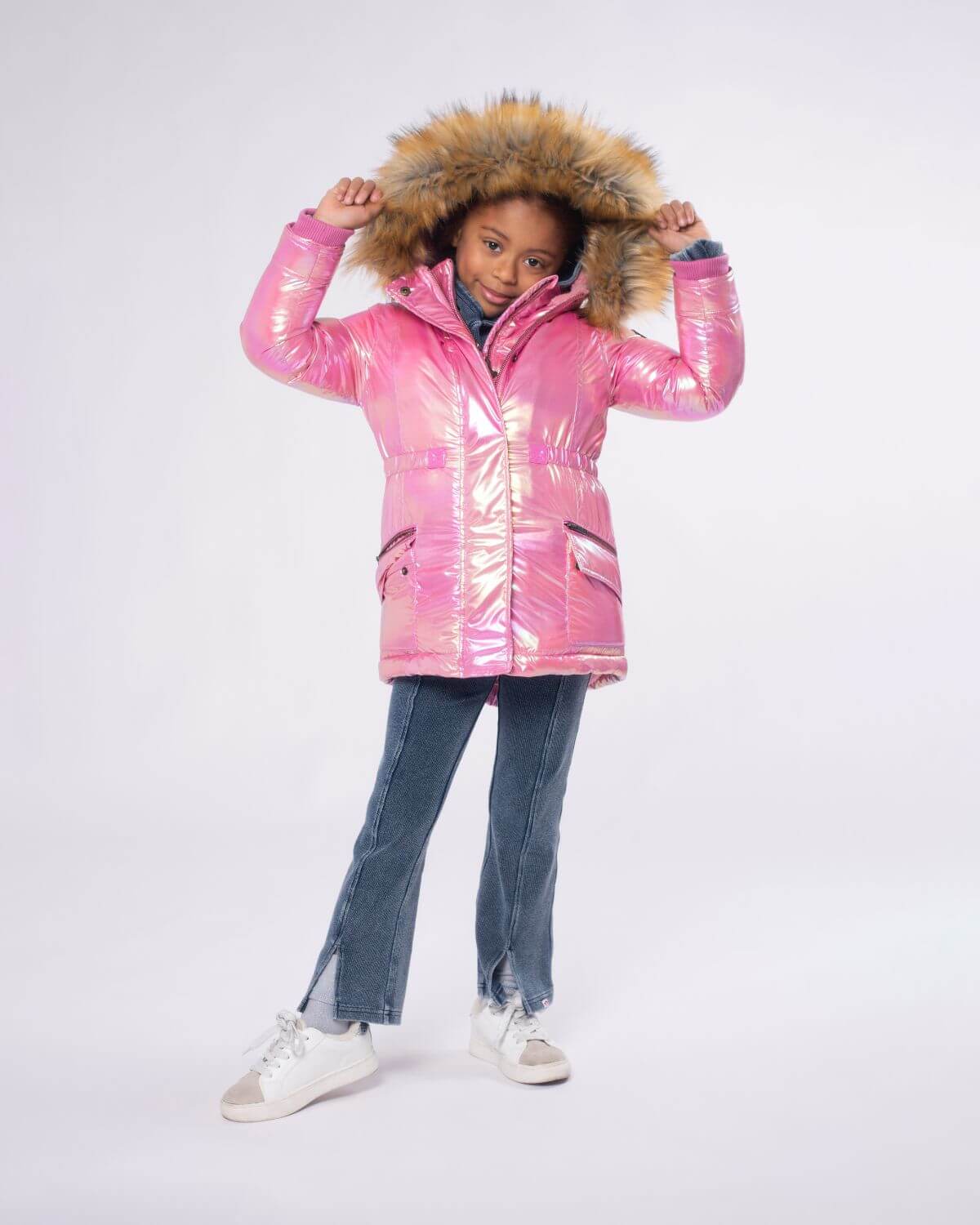 Confident kid in a radiant pink puffer coat with faux fur hood, standing stylishly in denim, ready for winter adventures.