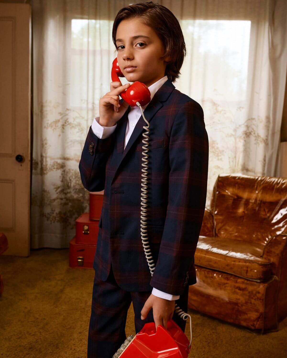 Trendy kid in a navy/cranberry plaid suit with a retro phone, showcasing stylish kids clothes vibes.