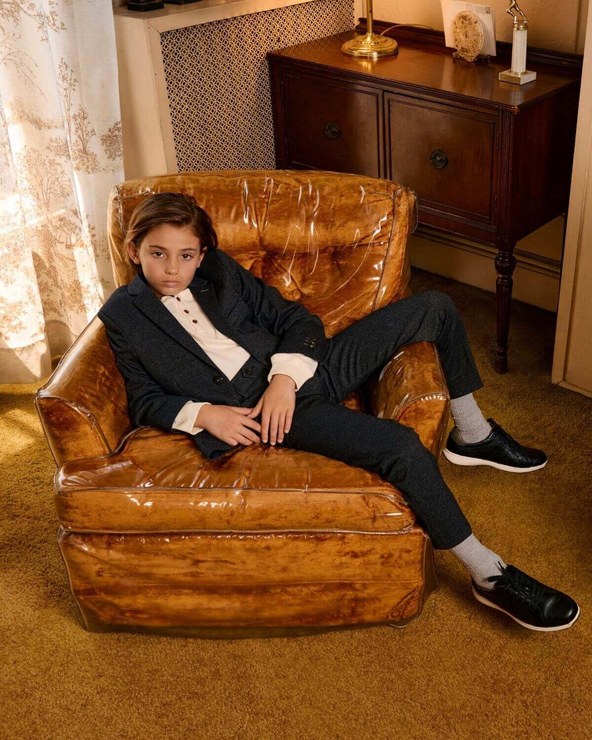 Stylish kid in black herringbone suit pants lounging confidently in a cozy vintage armchair, ready for fun!