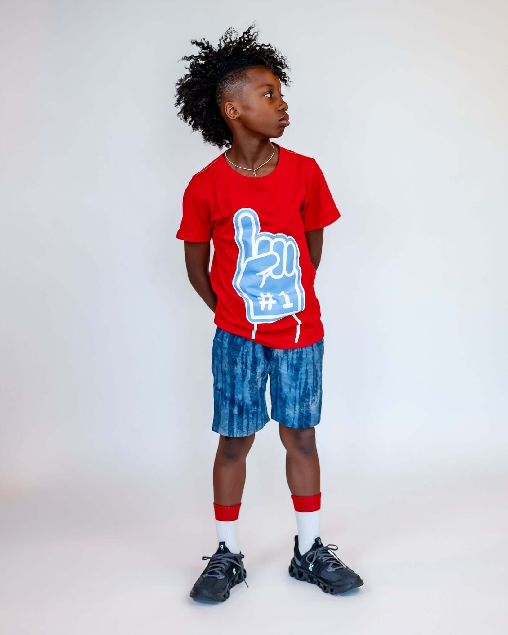 Child wearing a red t-shirt with a blue graphic and blue shorts on a white background