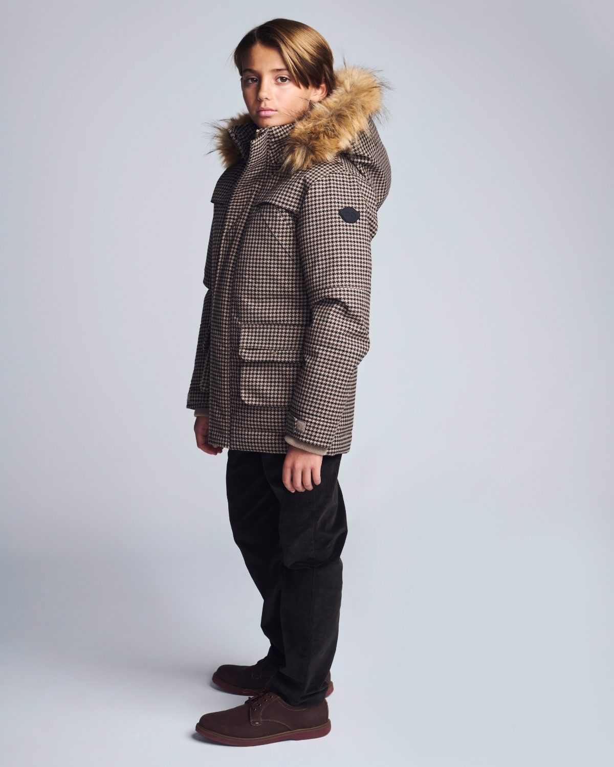 Person wearing a checkered coat with fur hood on a light gray background