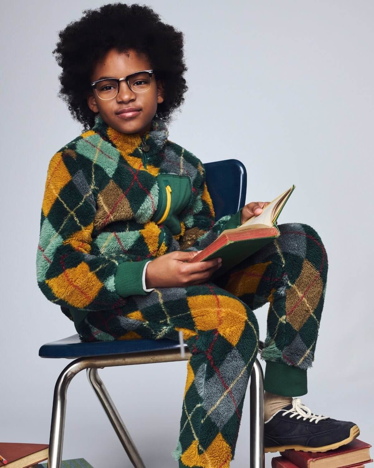 Person wearing a patterned outfit sitting on a chair with books around them.