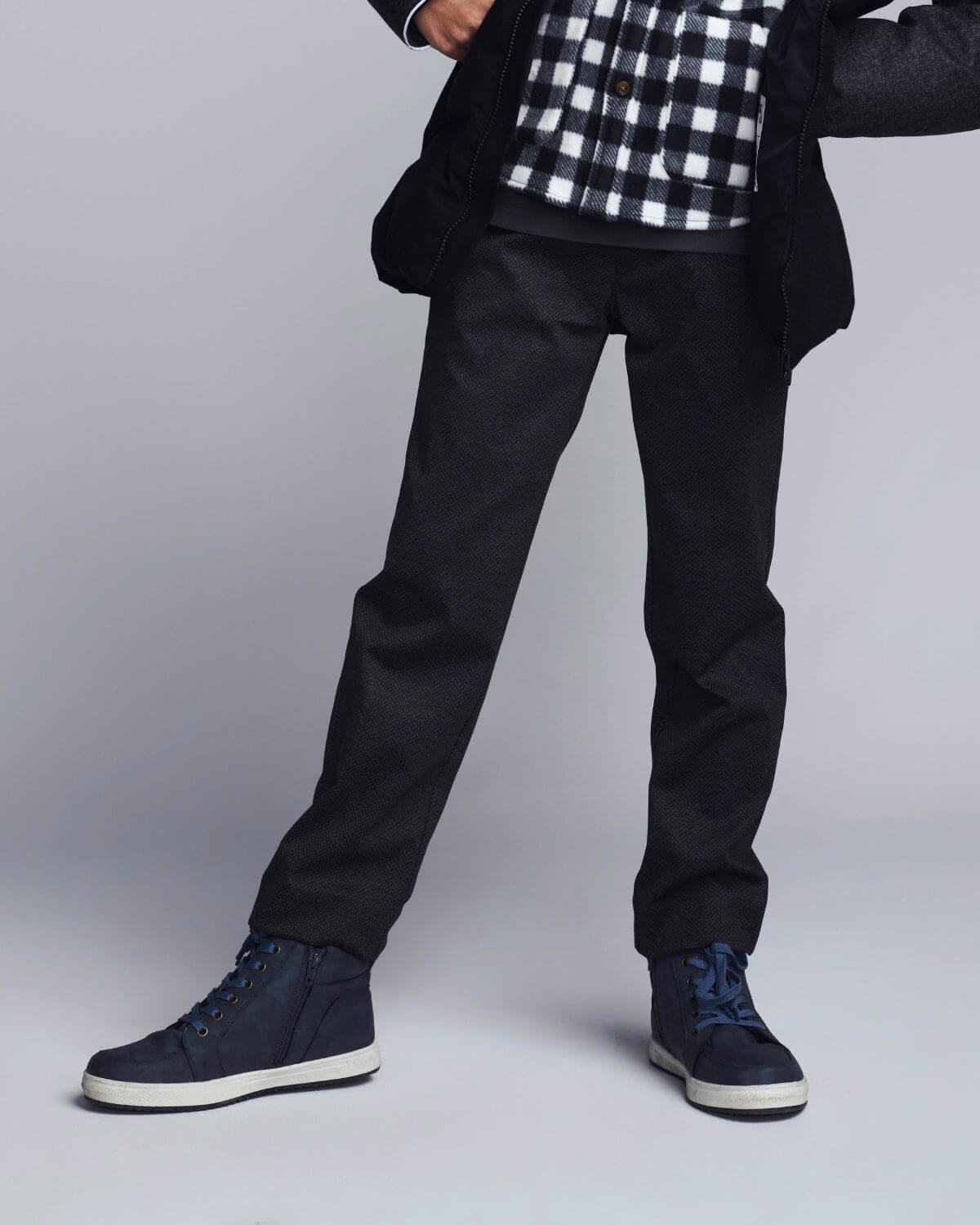 Person wearing black pants and navy blue shoes on a light gray background