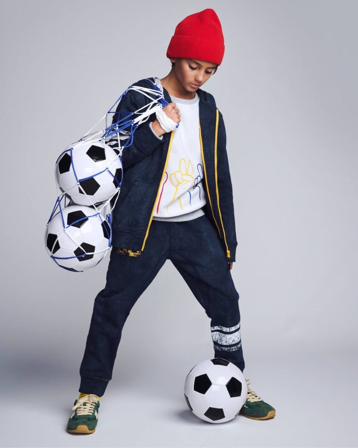 Child holding multiple soccer balls against a plain background