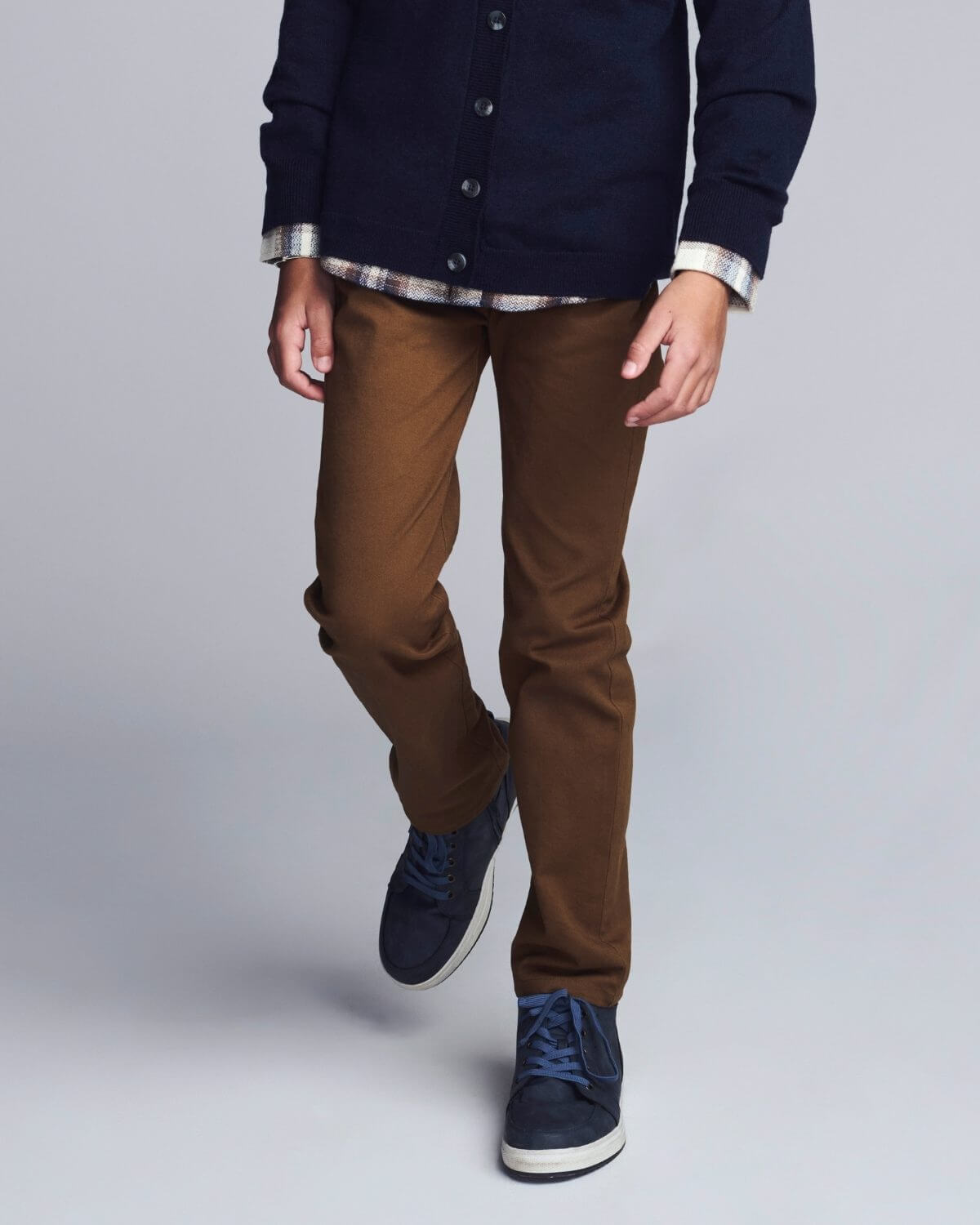 Person wearing a navy jacket, brown pants, and blue shoes on a light gray background