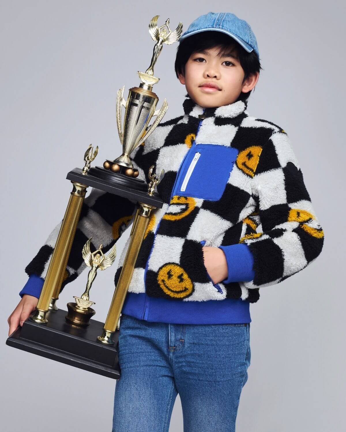 Child holding a large trophy with multiple awards on a plain background