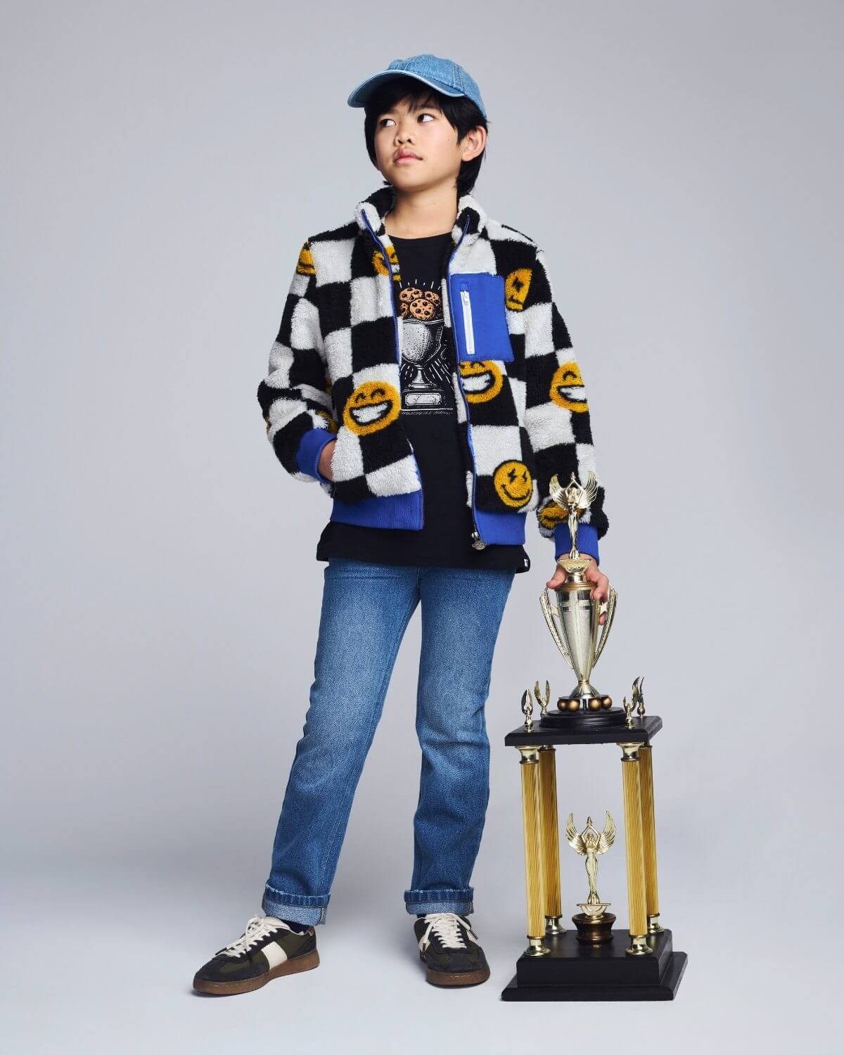 Person wearing a checkered jacket with smiley face patterns, holding a trophy on a gray background