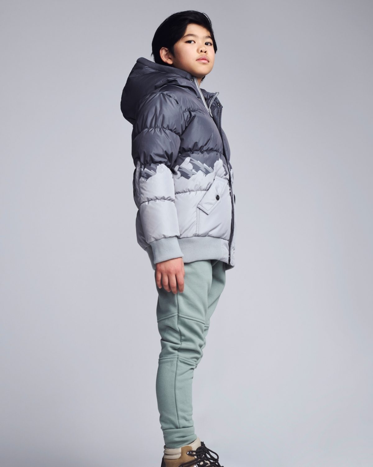 Child wearing a gray puffer jacket and light green pants on a gray background