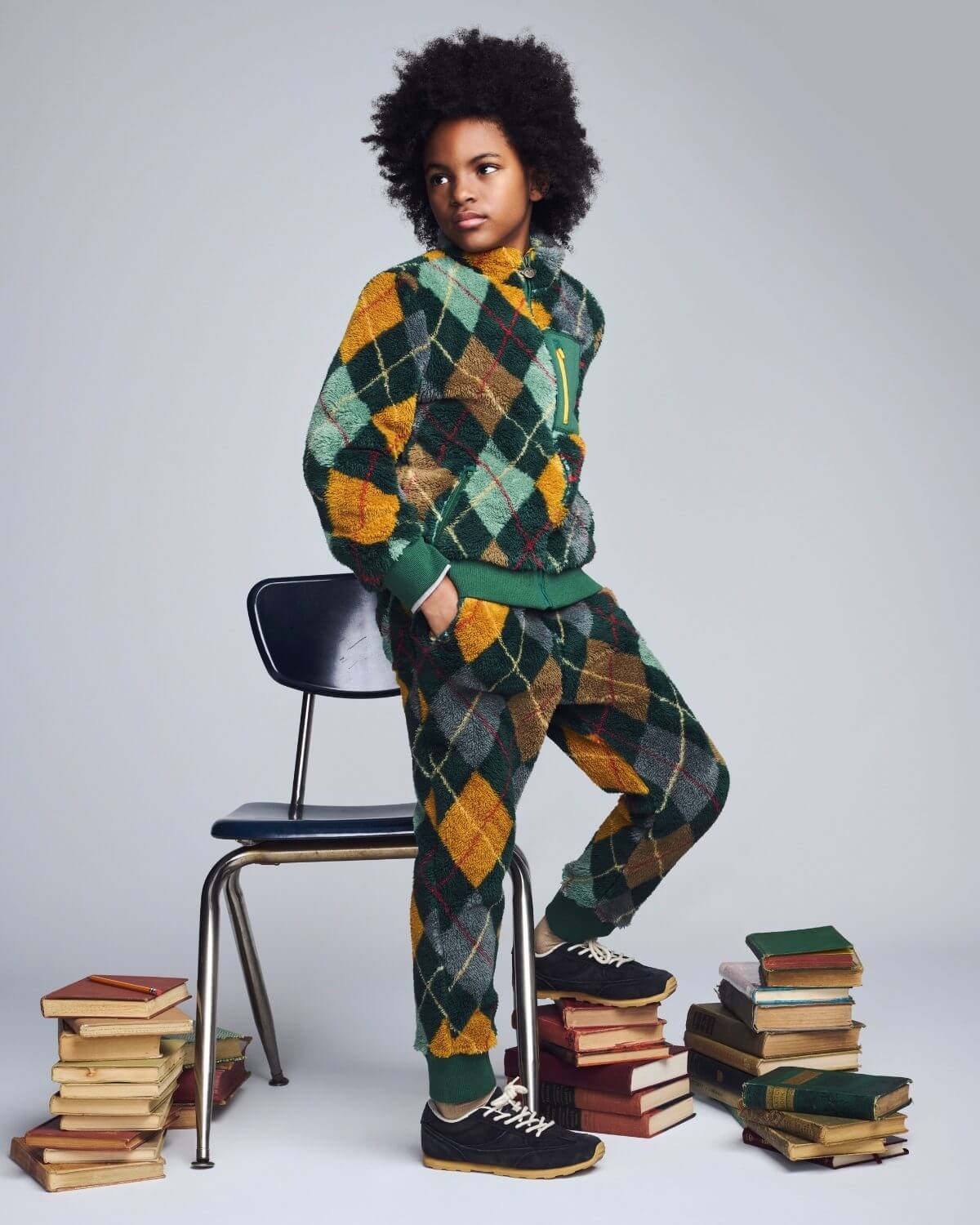 Person wearing a green and orange argyle patterned outfit sitting on a stack of books.