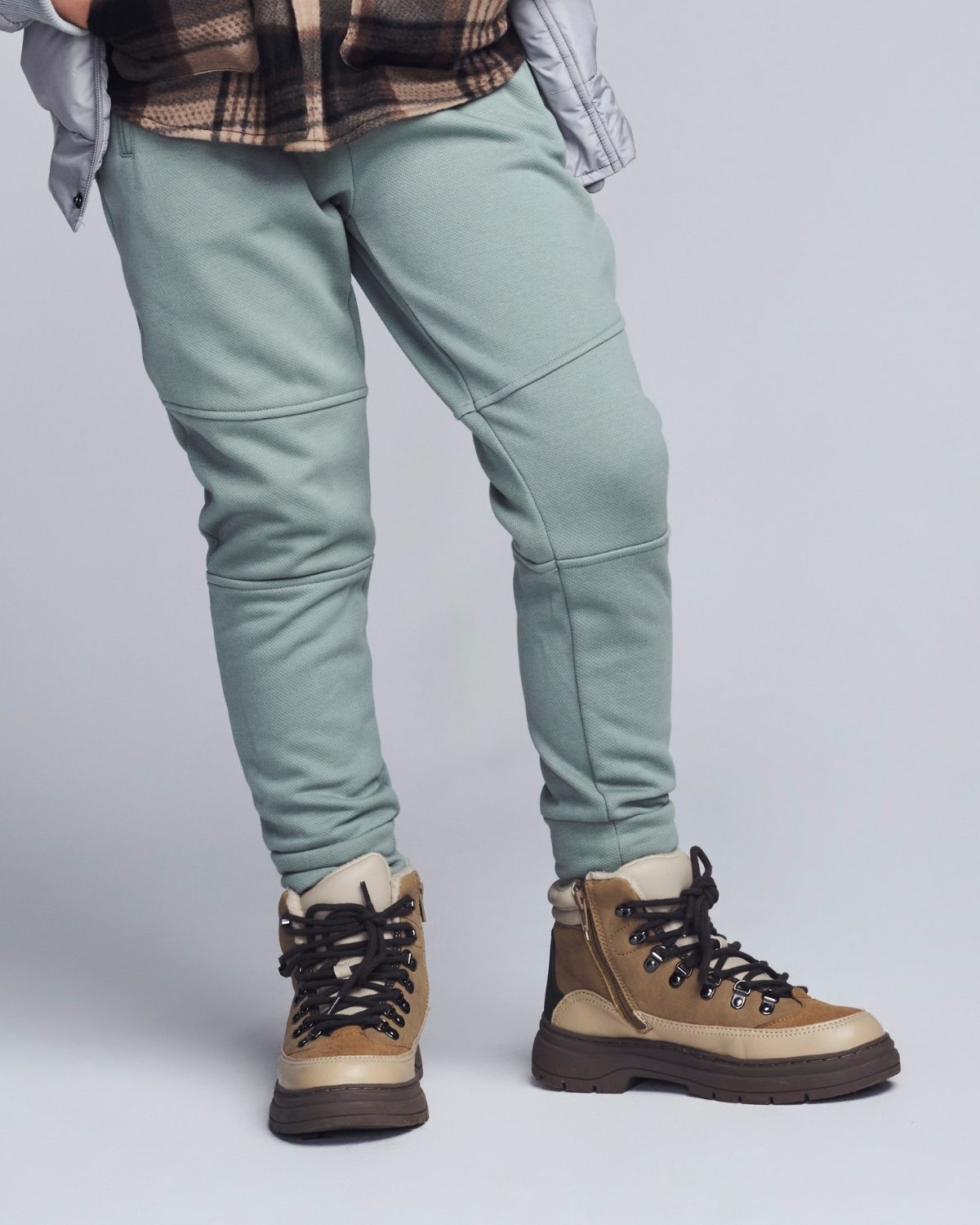 Person wearing light green pants and brown hiking boots on a plain background