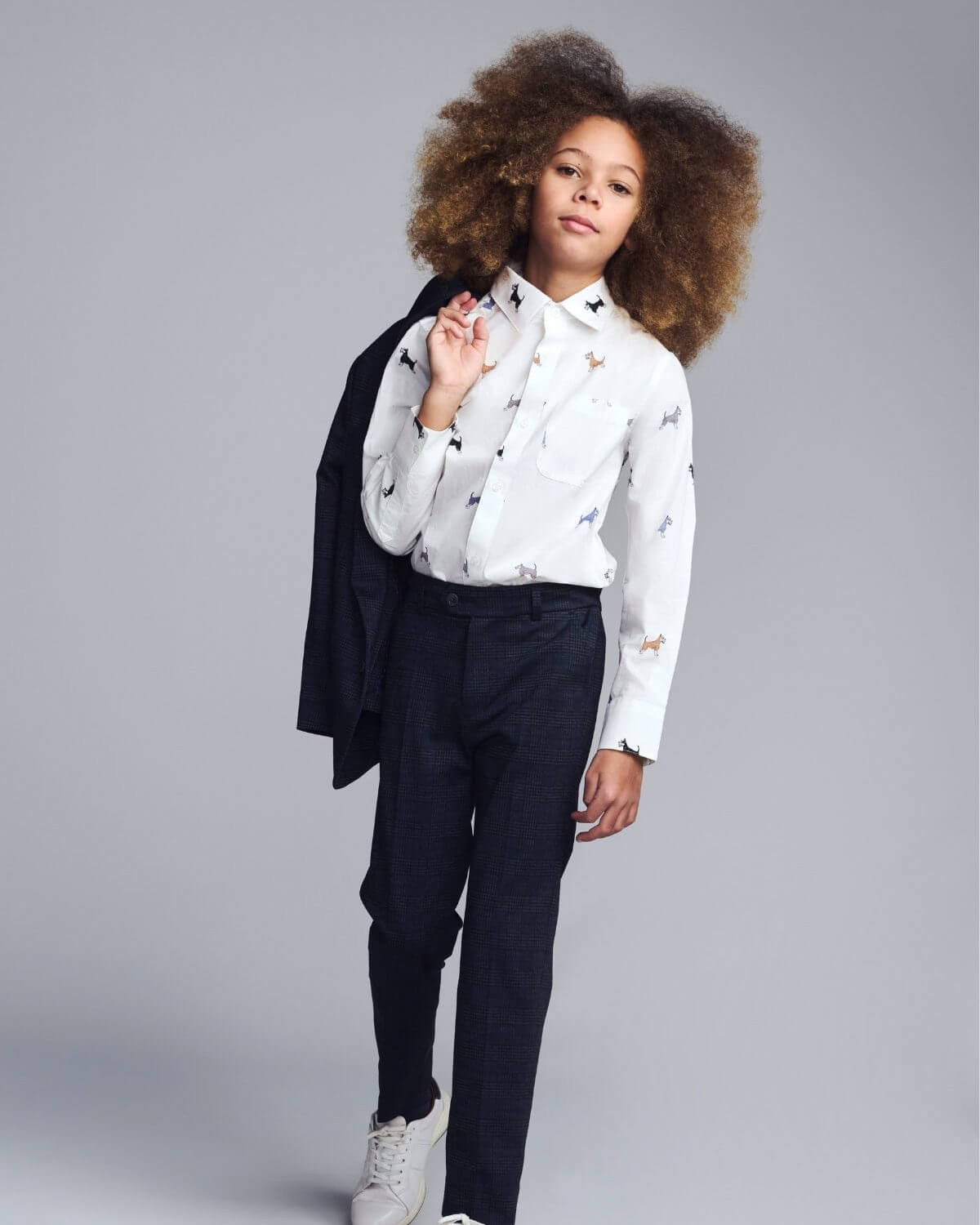 Child wearing a white shirt with black patterns and dark pants on a gray background