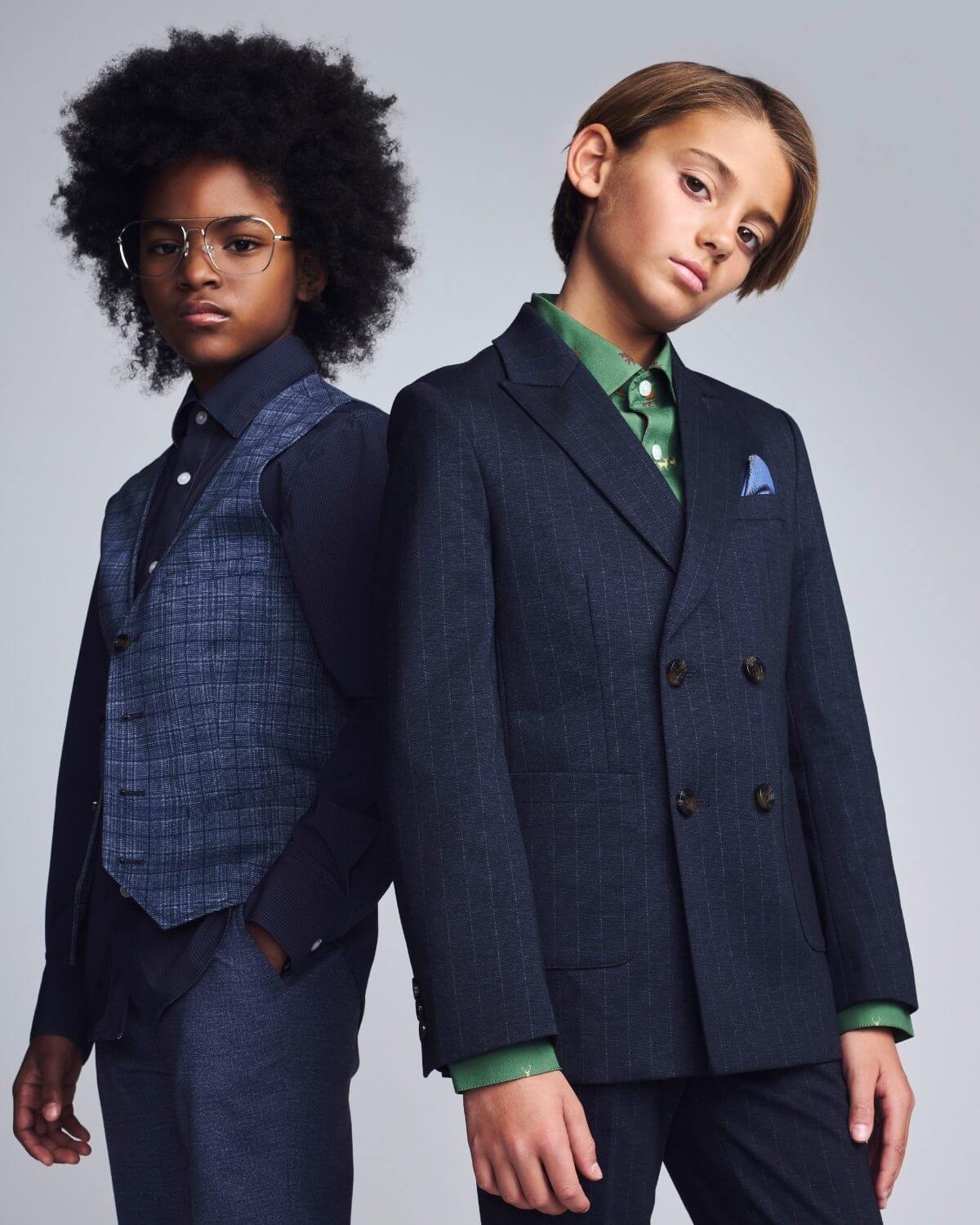 Two children wearing formal suits against a plain background