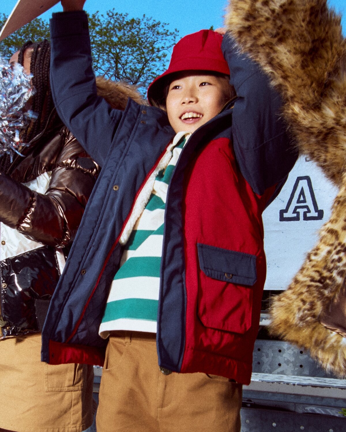 Child wearing a colorful jacket and red hat with a blue sky background