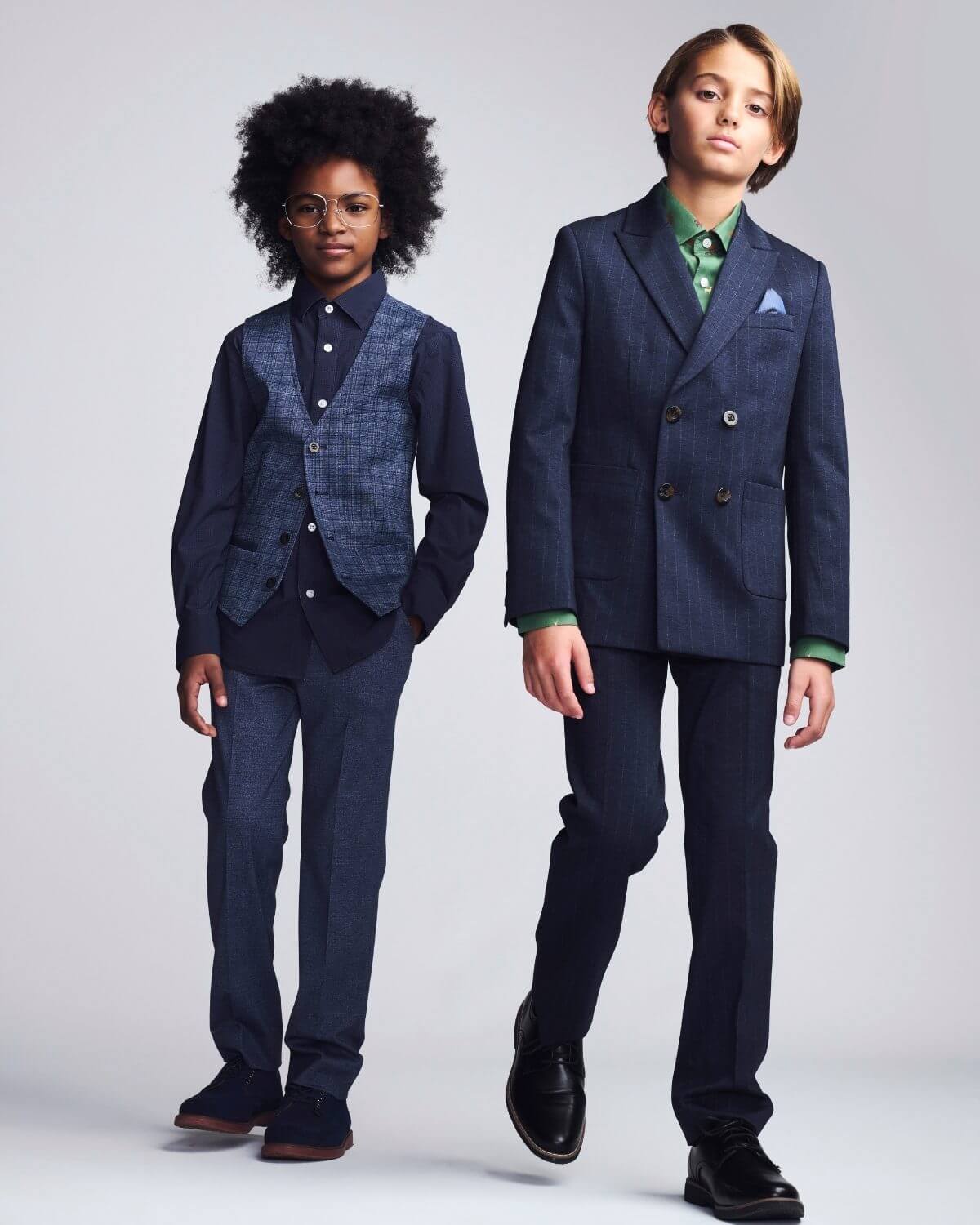 Two children wearing formal suits on a plain background
