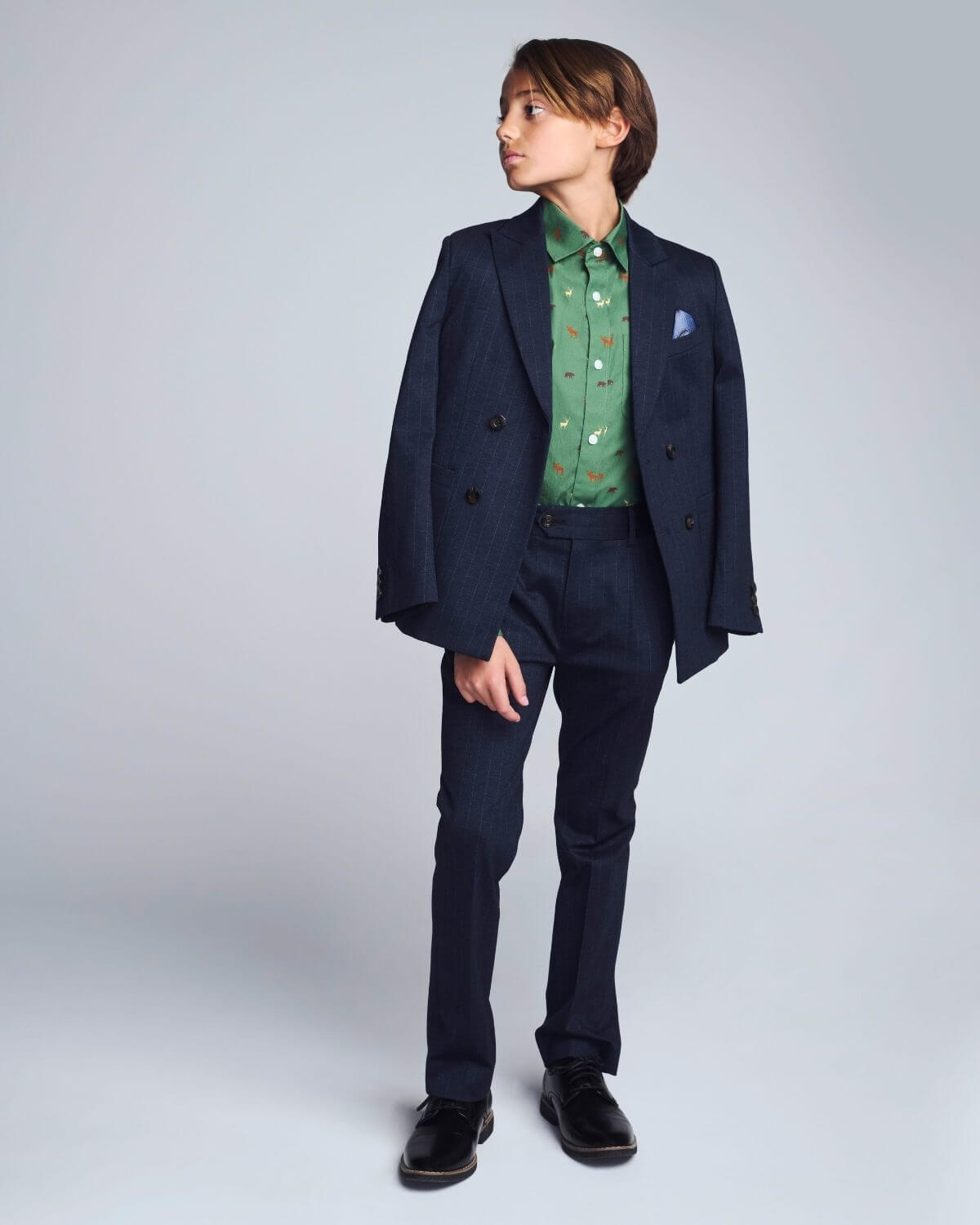 Person wearing a navy suit with a green patterned shirt on a light gray background