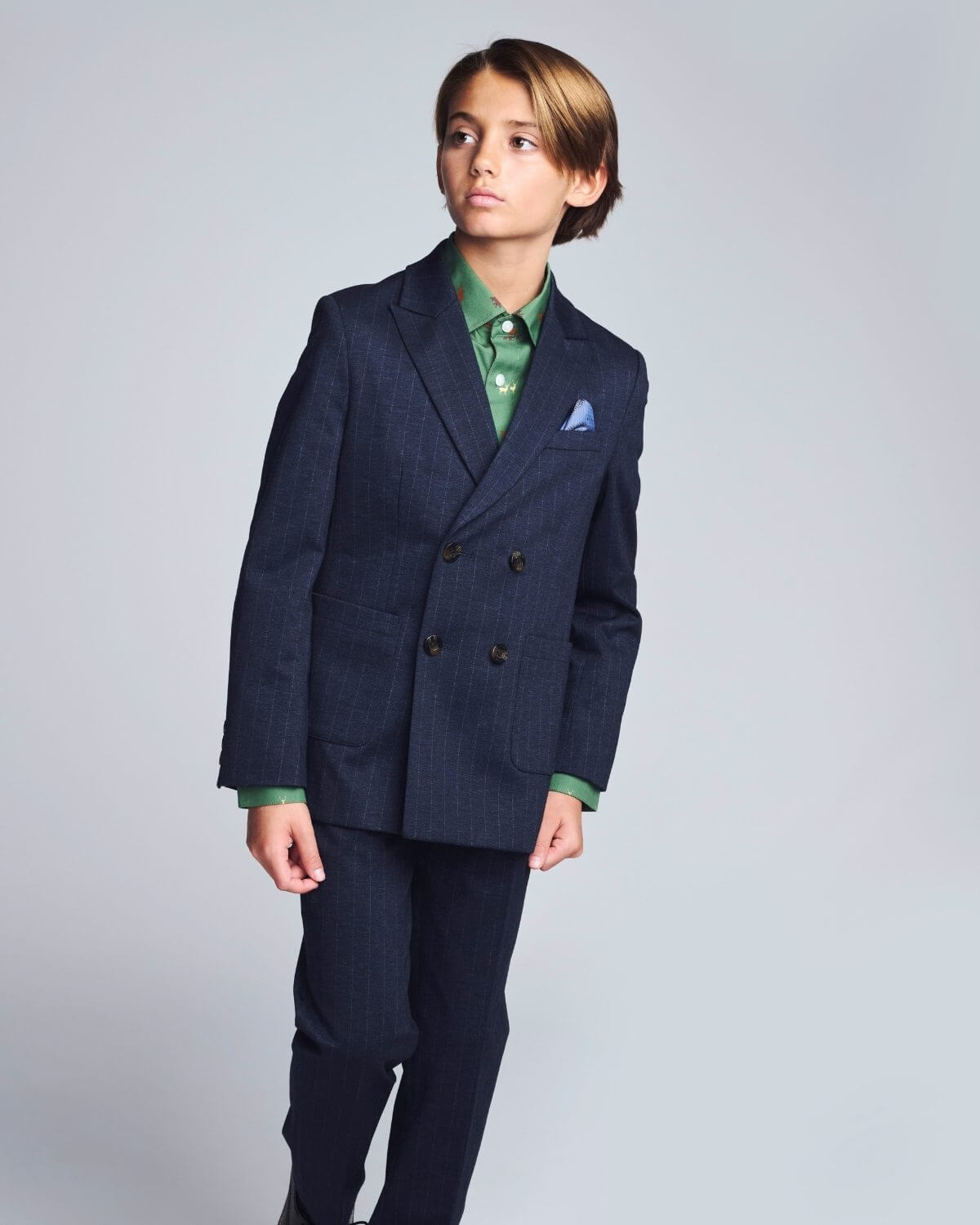Young boy wearing a navy suit with a green shirt and pocket square on a gray background