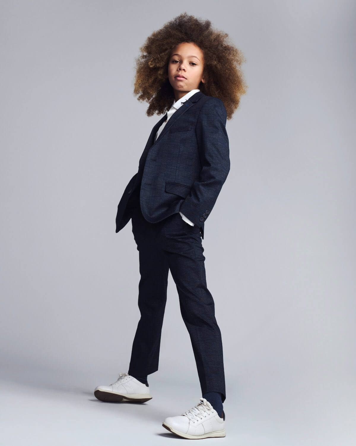 Person wearing a navy suit with white sneakers on a gray background
