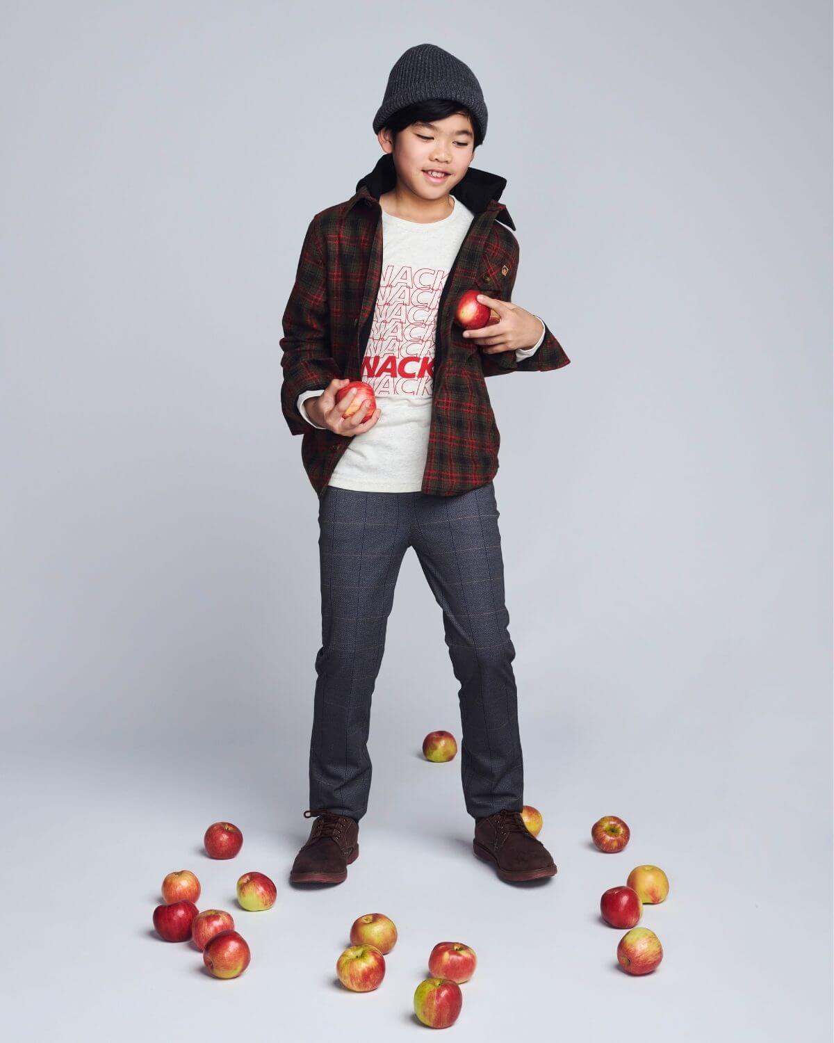 Child holding apples with a scattered pile on a plain background