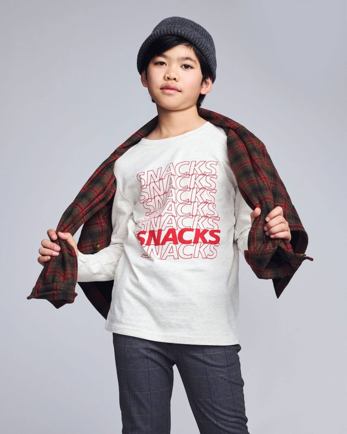 Child wearing a white t-shirt with 'SNACKS' text and a plaid shirt over shoulders on a gray background