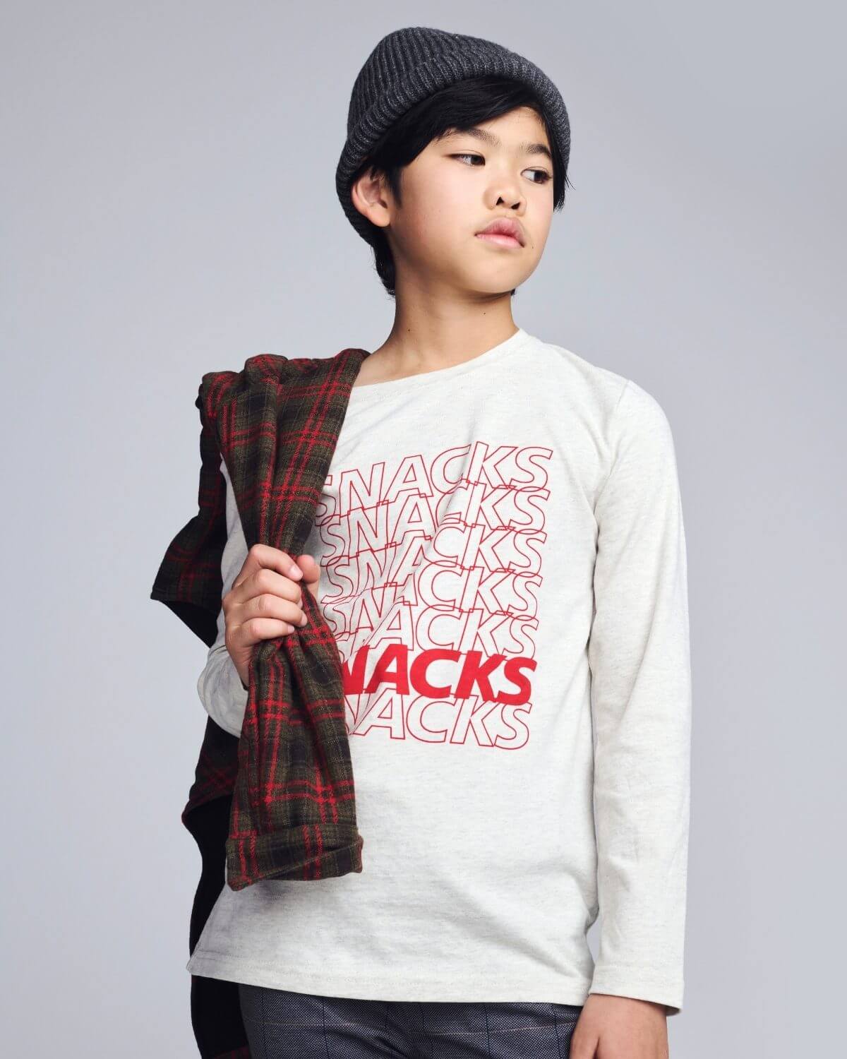 Child wearing a white sweatshirt with 'SNACKS' text, holding a plaid scarf on a gray background