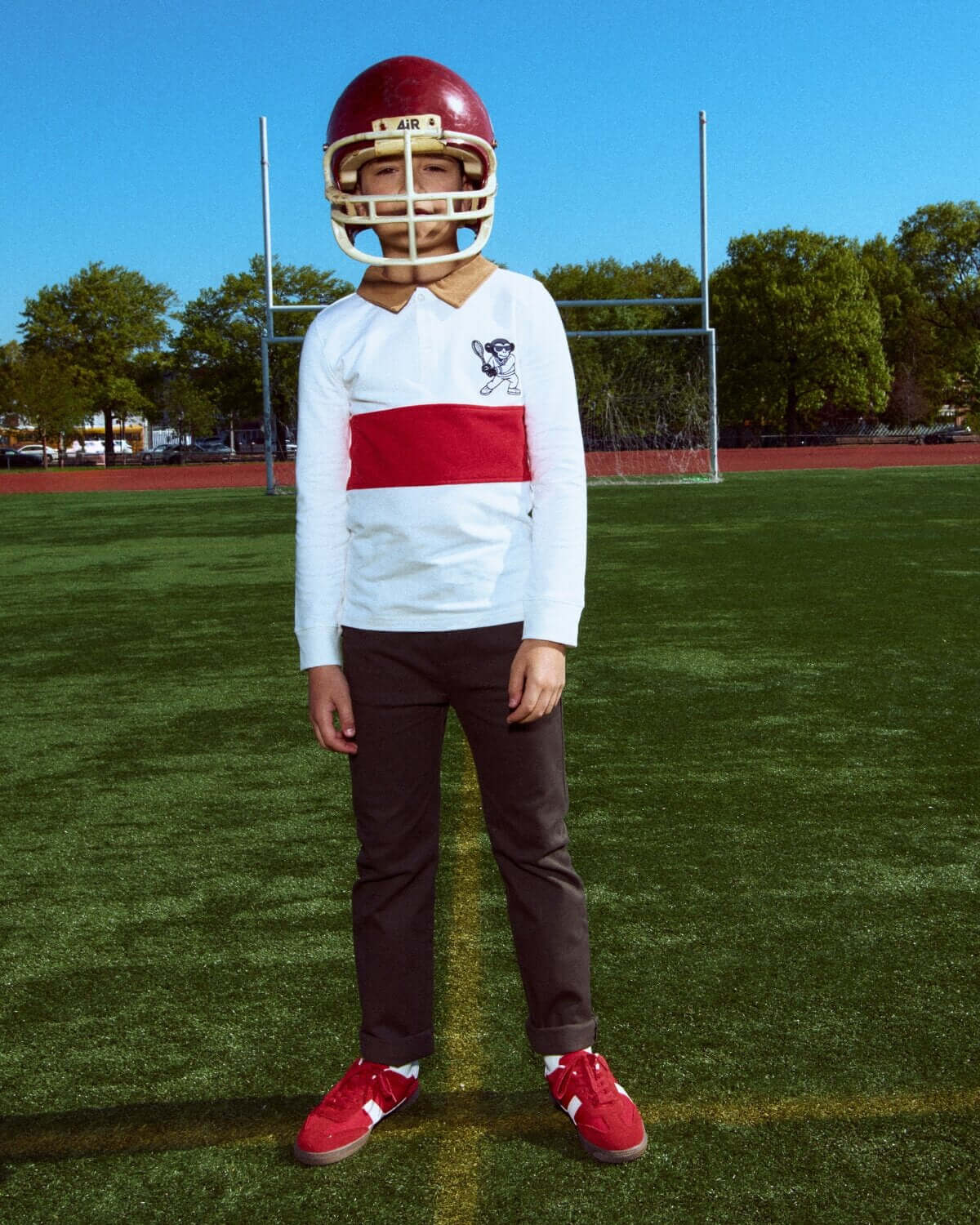 Person wearing a football helmet, white jersey with red stripe, and dark pants on a sports field.
