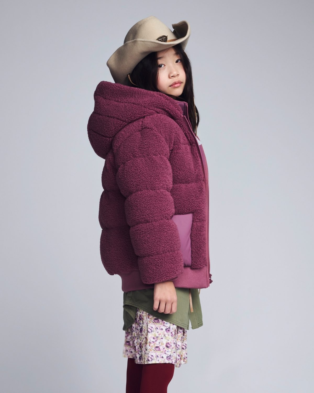 Child wearing a purple puffer jacket and beige hat on a plain background