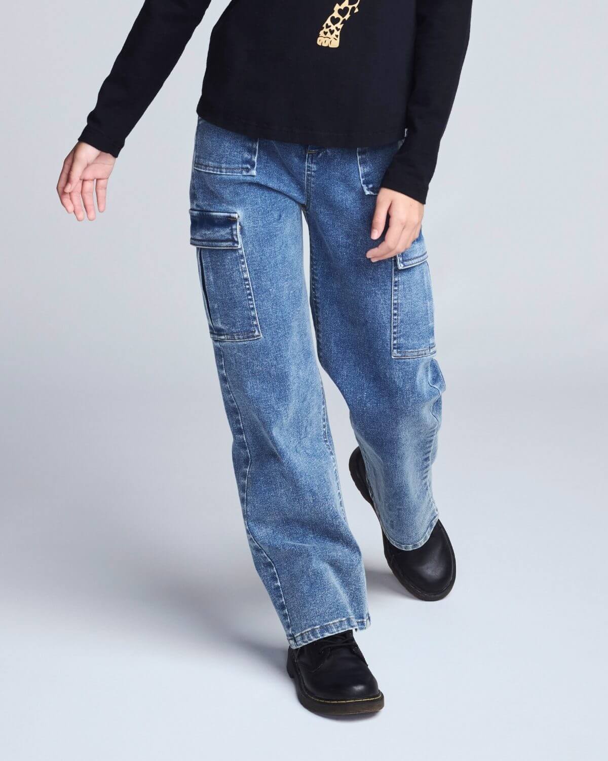 Person wearing blue jeans and black shoes on a light gray background