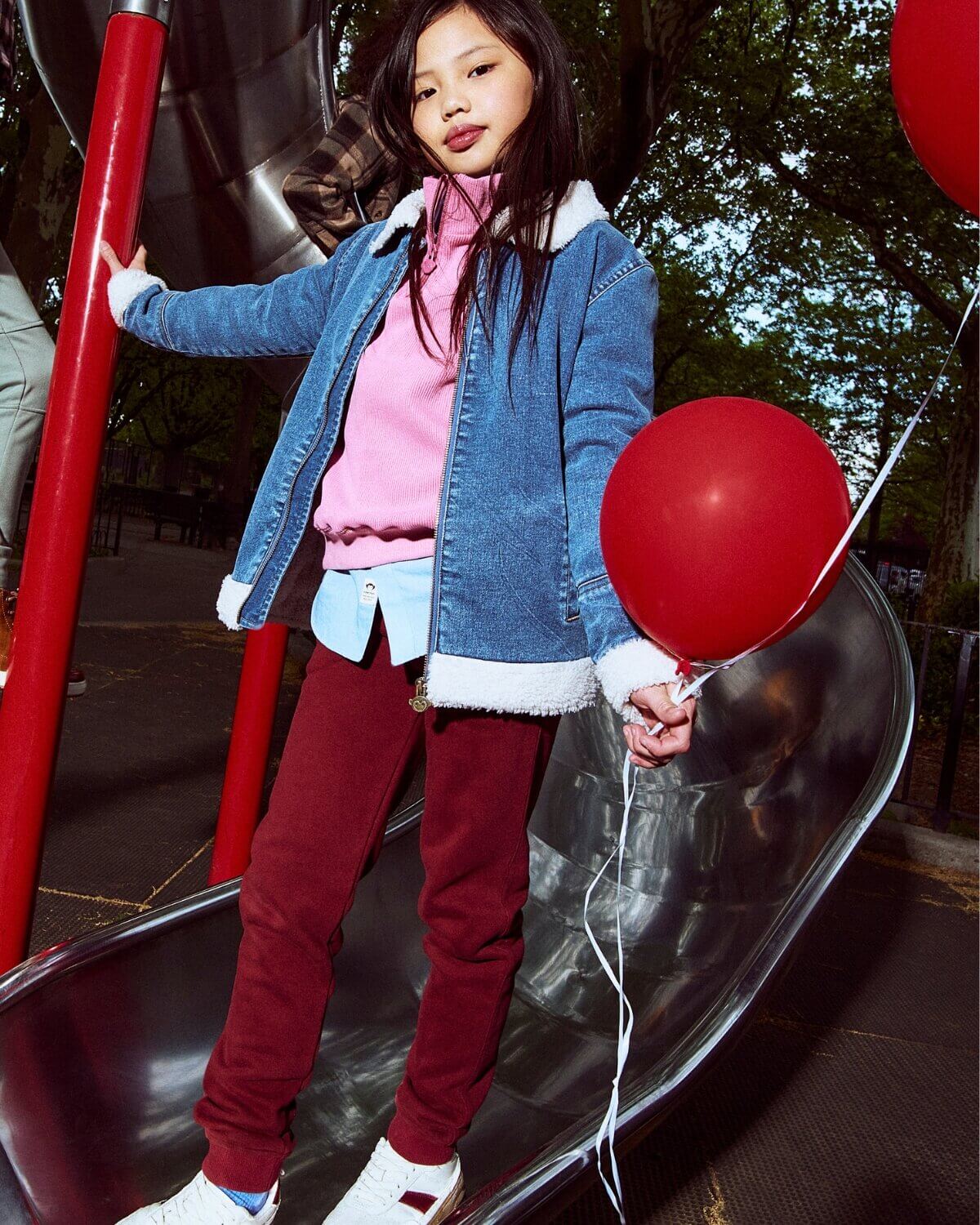 Child on a playground slide holding a red balloon