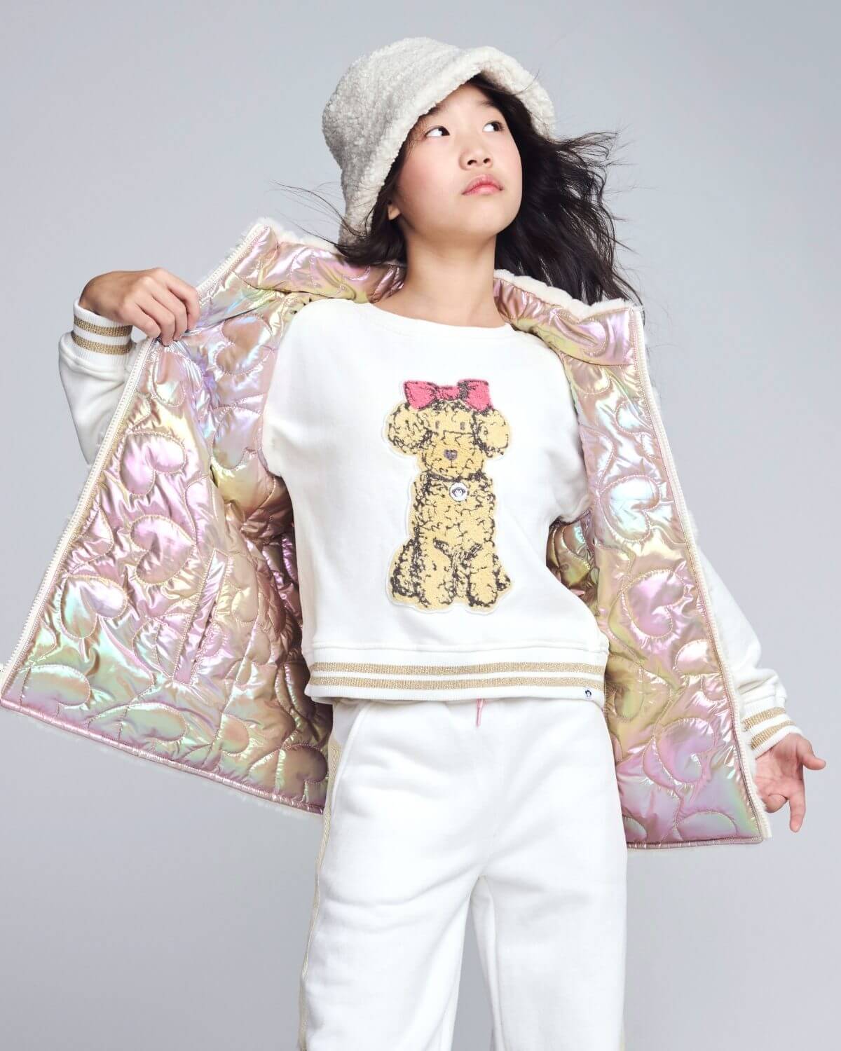 Person wearing a white sweater with a teddy bear design and a colorful quilted jacket on a gray background