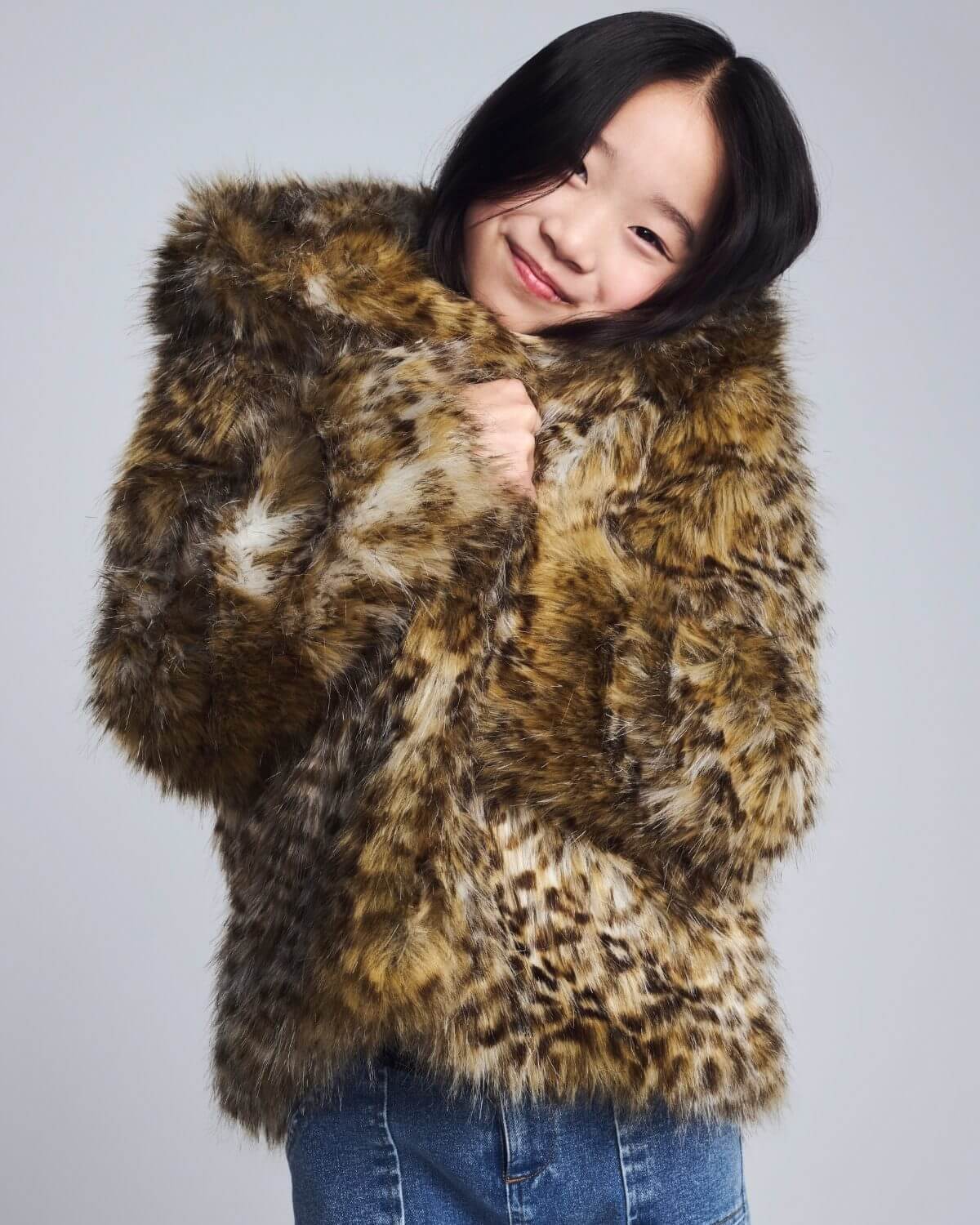 Girl wearing a leopard print fur coat against a plain background