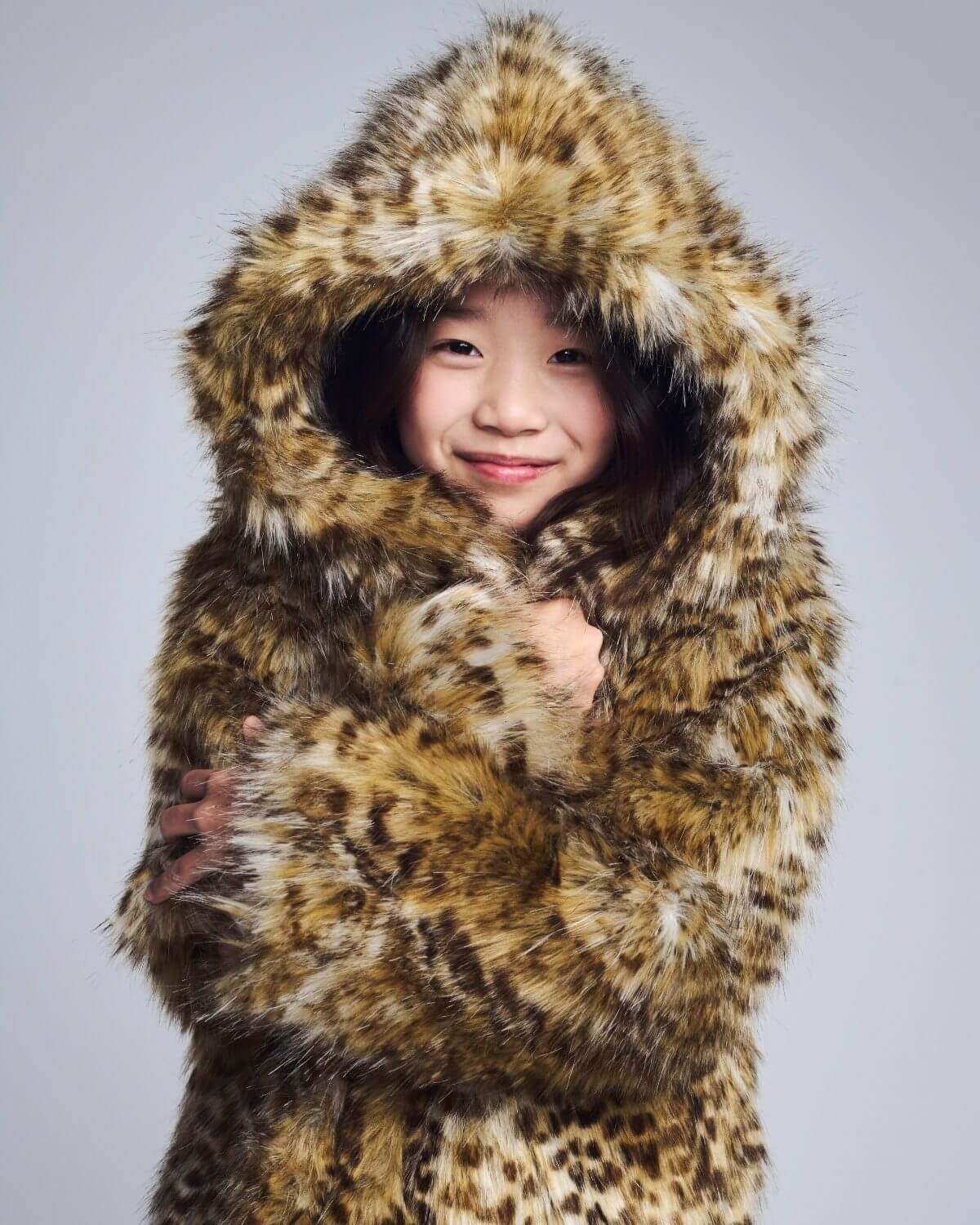 Child wearing a fur-lined coat with a hood on a gray background