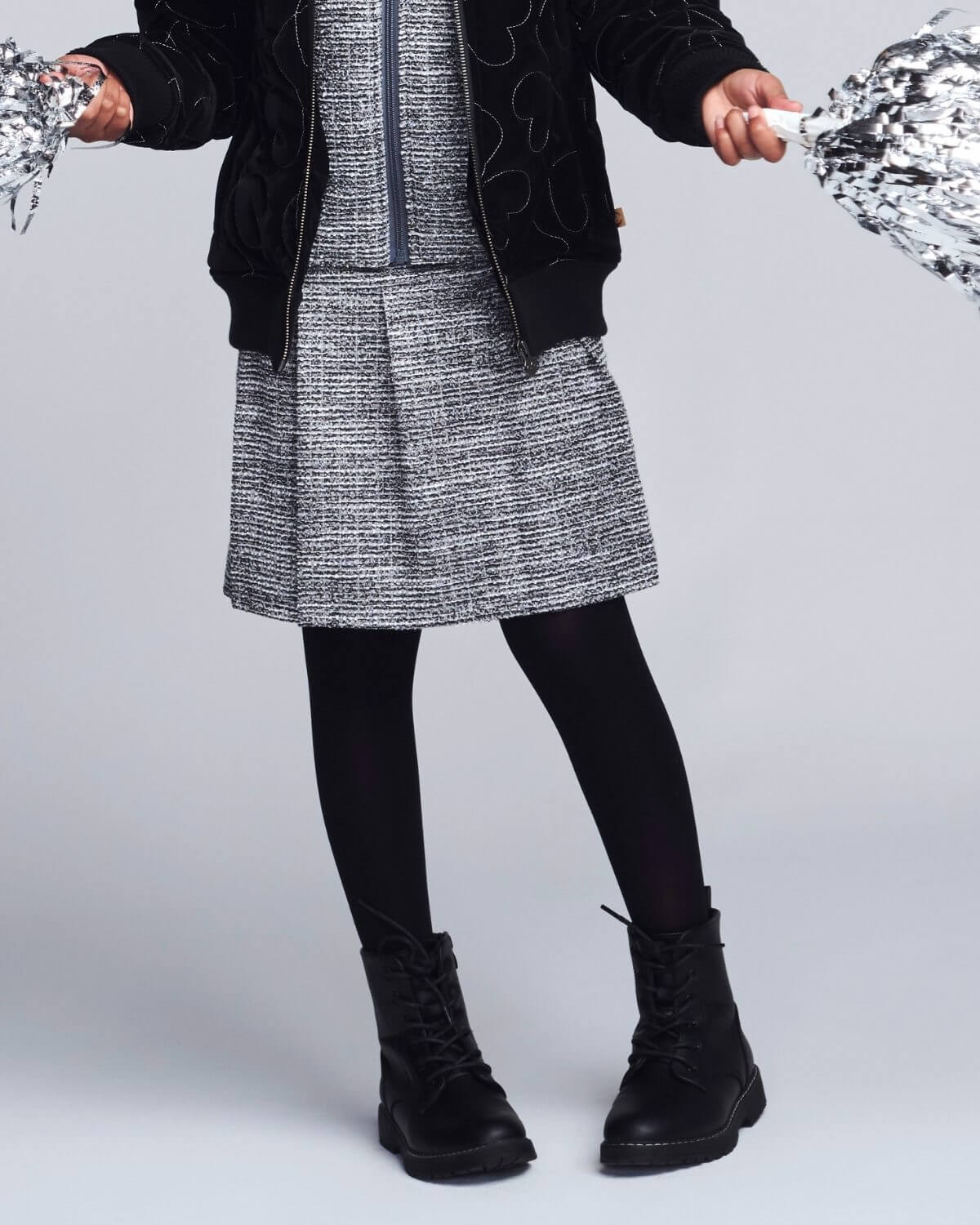 Person wearing a black and white patterned dress with black boots on a light gray background