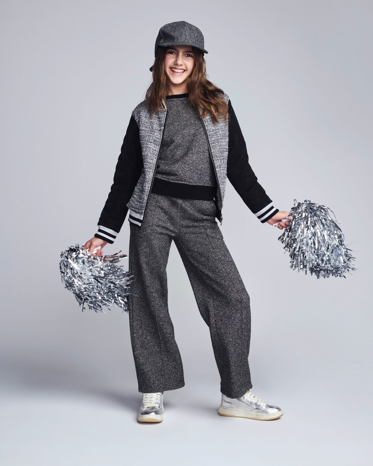 Person in gray and black varsity outfit with pom-poms on a light gray background