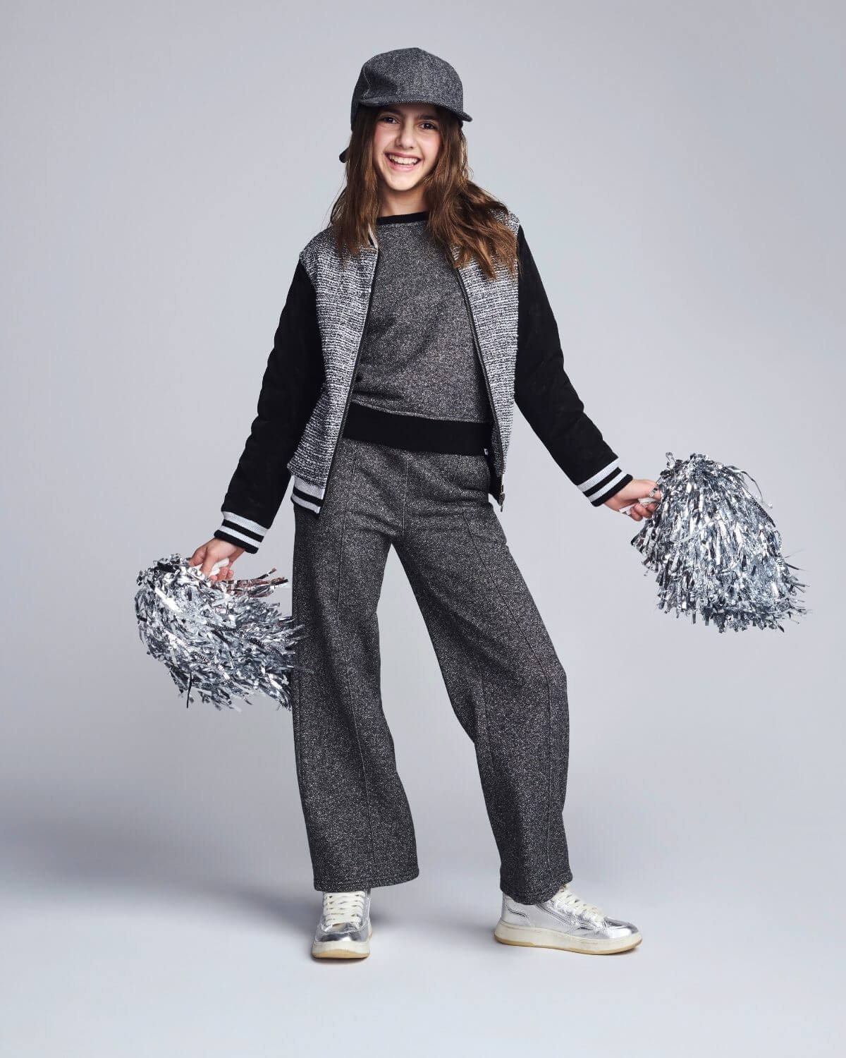 Person in gray and black varsity outfit with pom-poms on a light gray background
