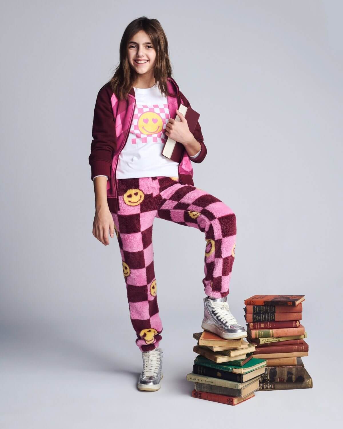 Person wearing a checkered outfit with smiley face patterns, standing on a stack of books against a plain background.