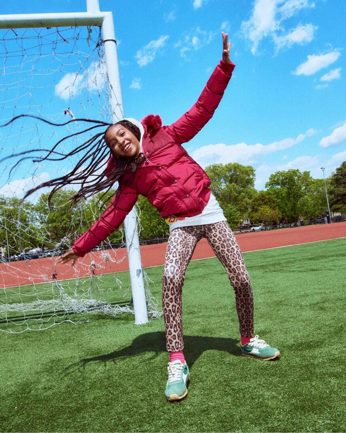 Person in red jacket and leopard print pants standing on a sports field with a goalpost in the background.