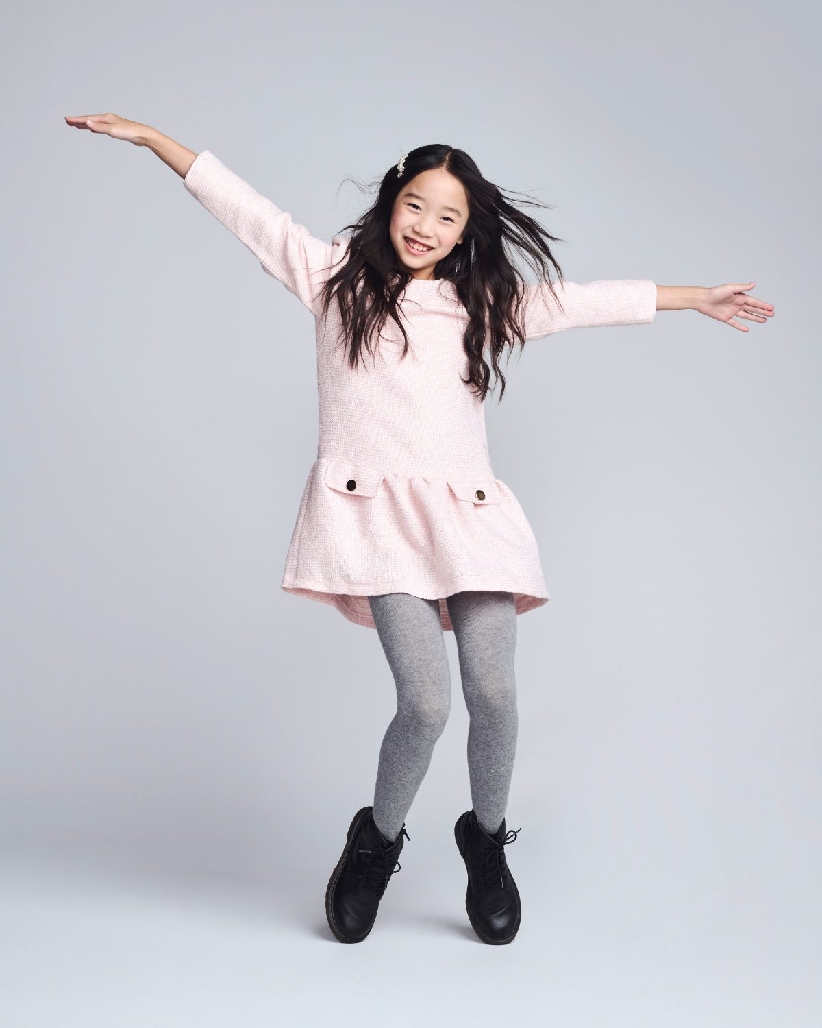 Young girl in a pink dress with arms outstretched on a plain background