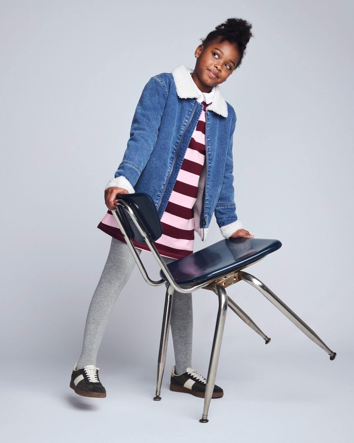 Child holding a chair against a plain background