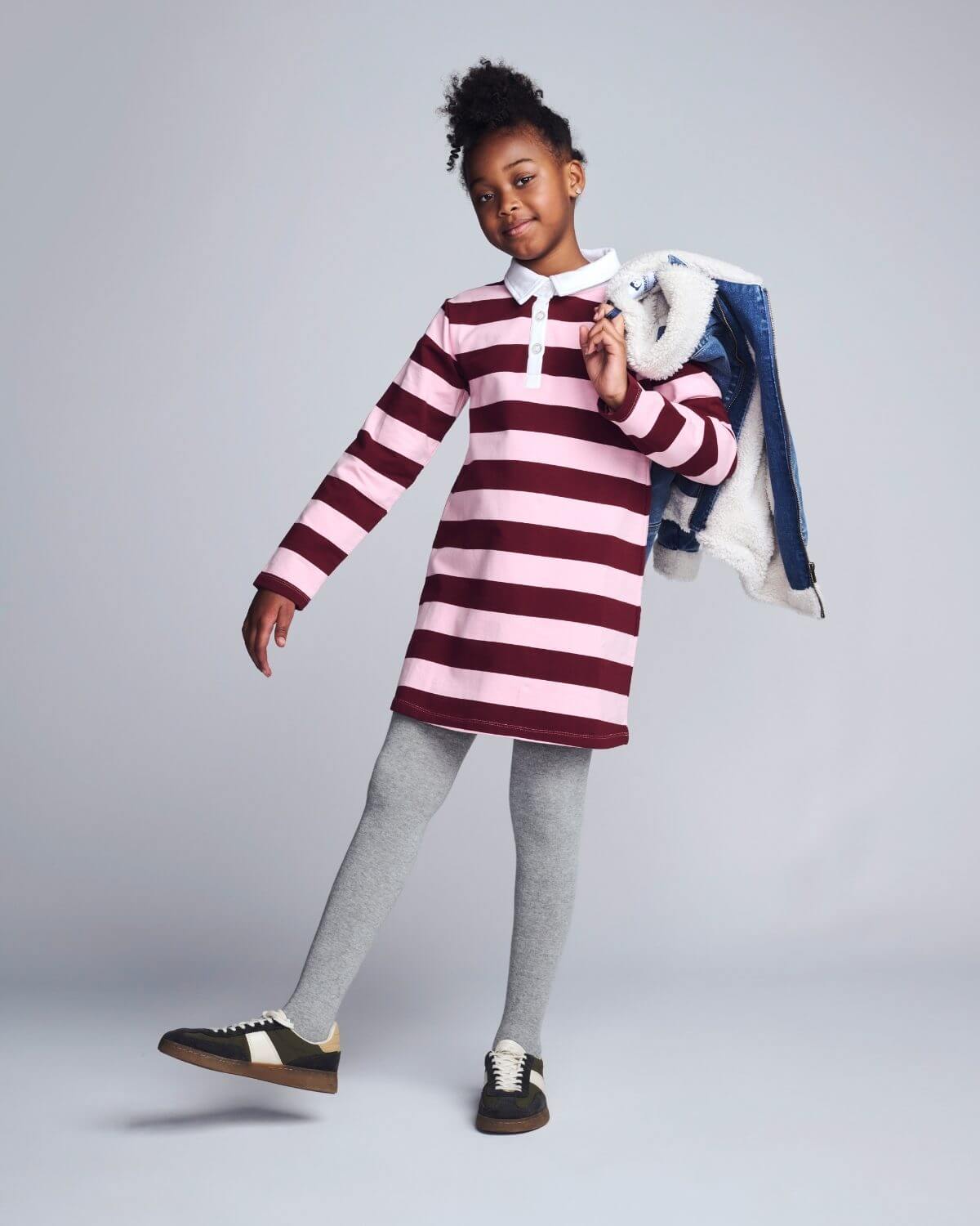 Child wearing a striped dress with gray leggings and black shoes on a plain background