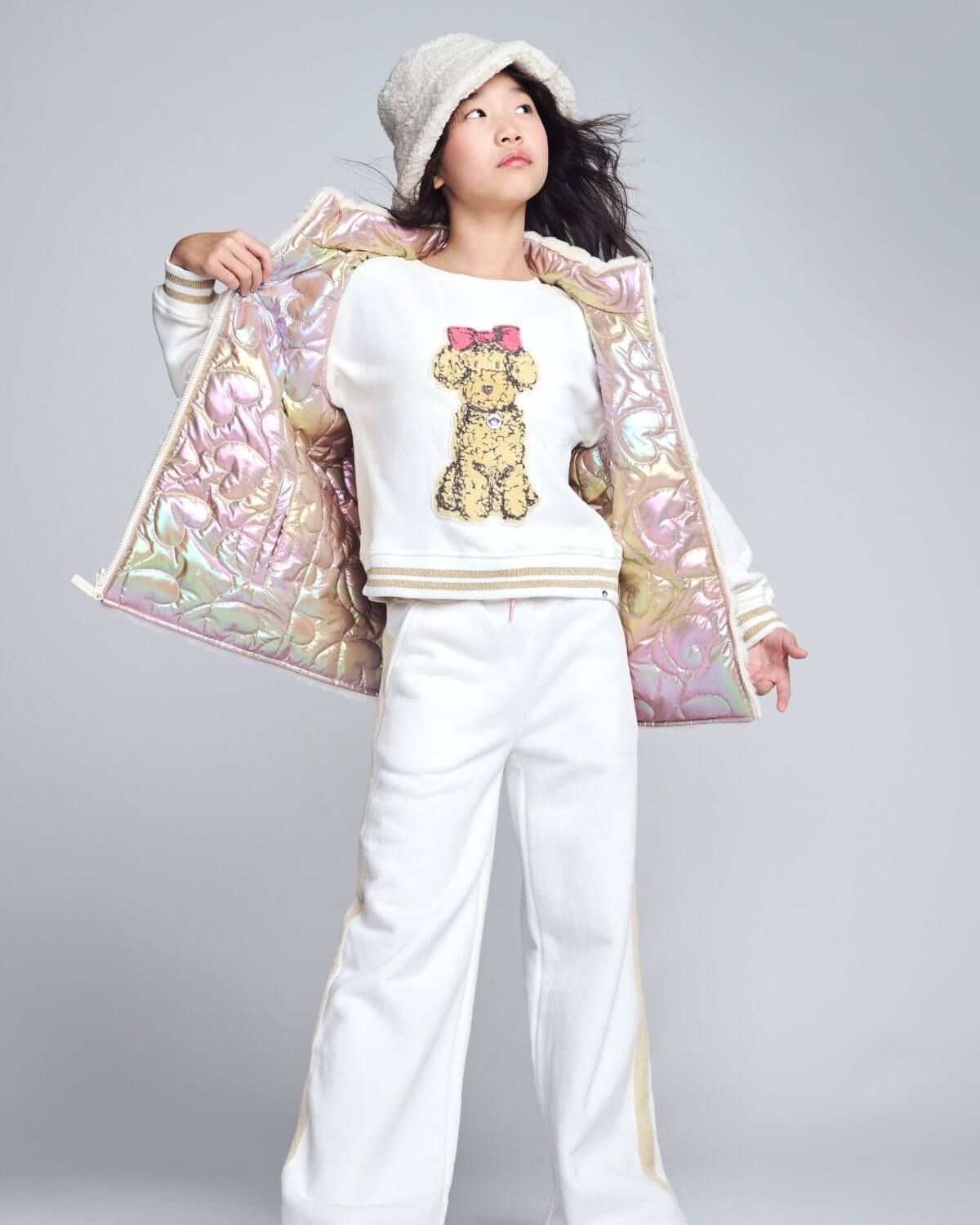 Person wearing a white outfit with a teddy bear design, holding a colorful bag on a gray background
