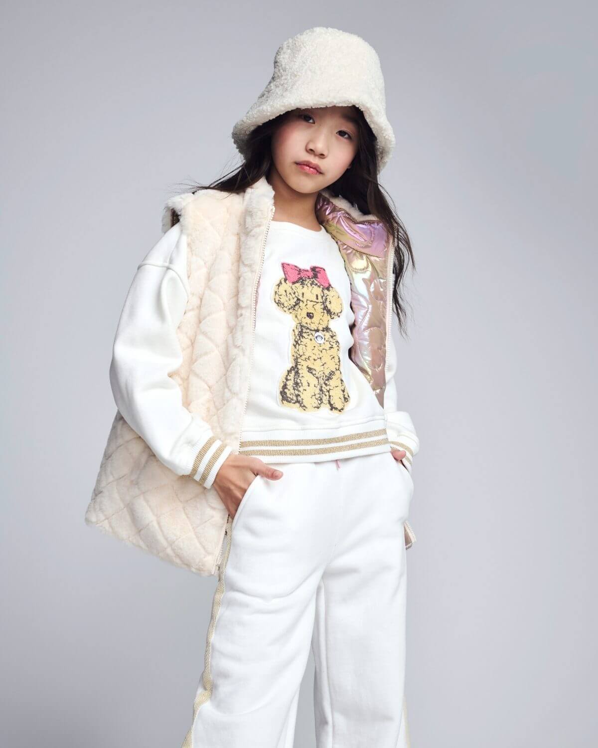 Child wearing a white outfit with a fur vest and hat on a gray background